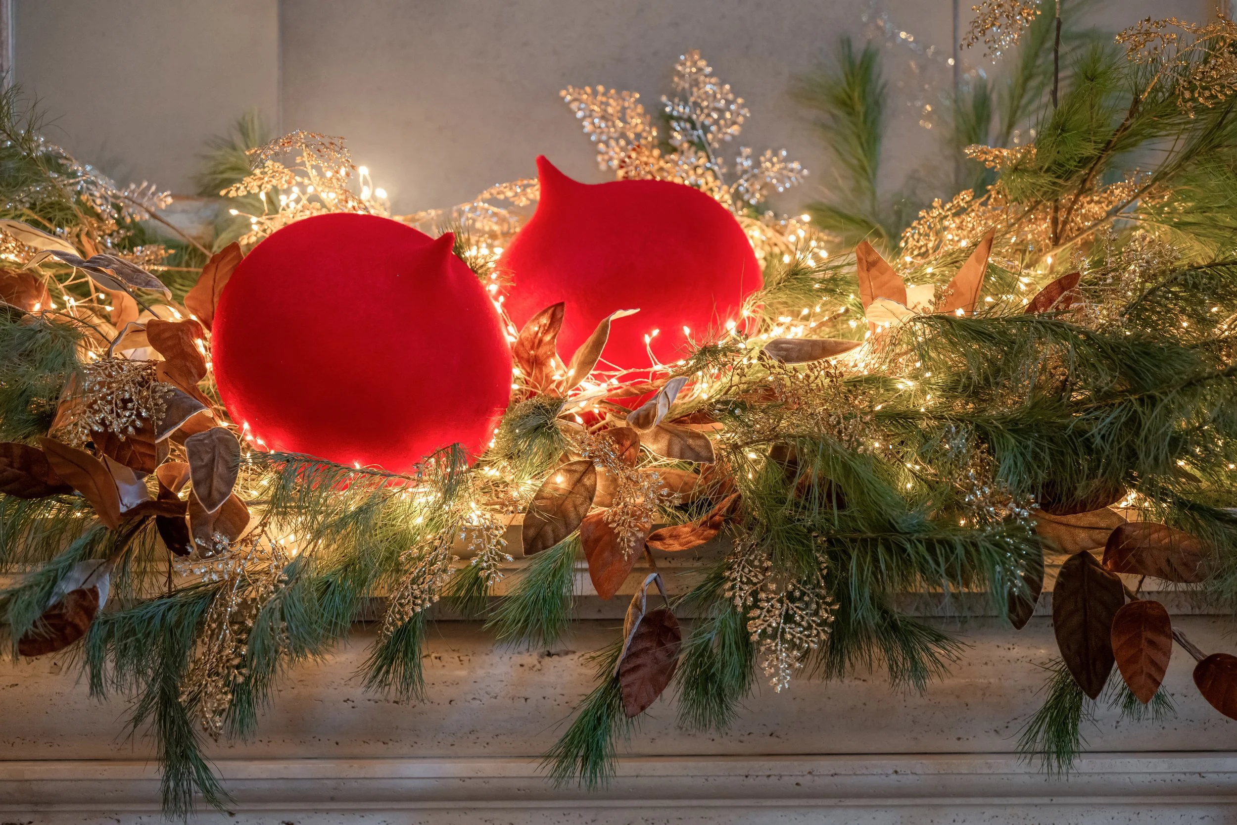 Decorative holiday Christmas garland with greenery, gold accents, fairy lights, and two large red ornaments.