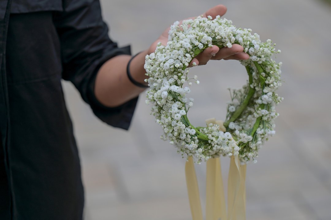 Person holding a white flower wreath with ribbons hanging from it.