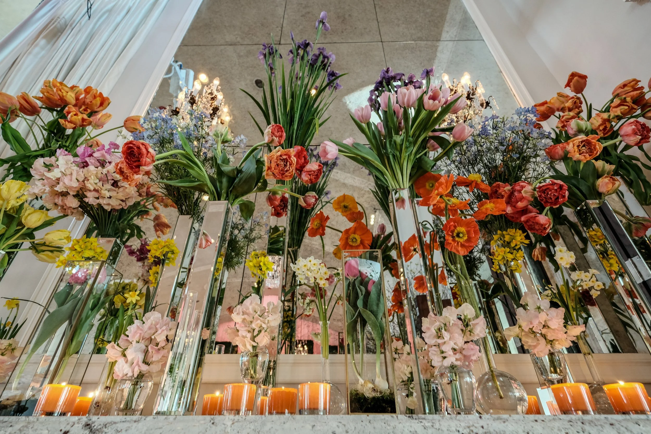 Arrangement of colorful flowers in glass vases with candles at the base, photographed from below.