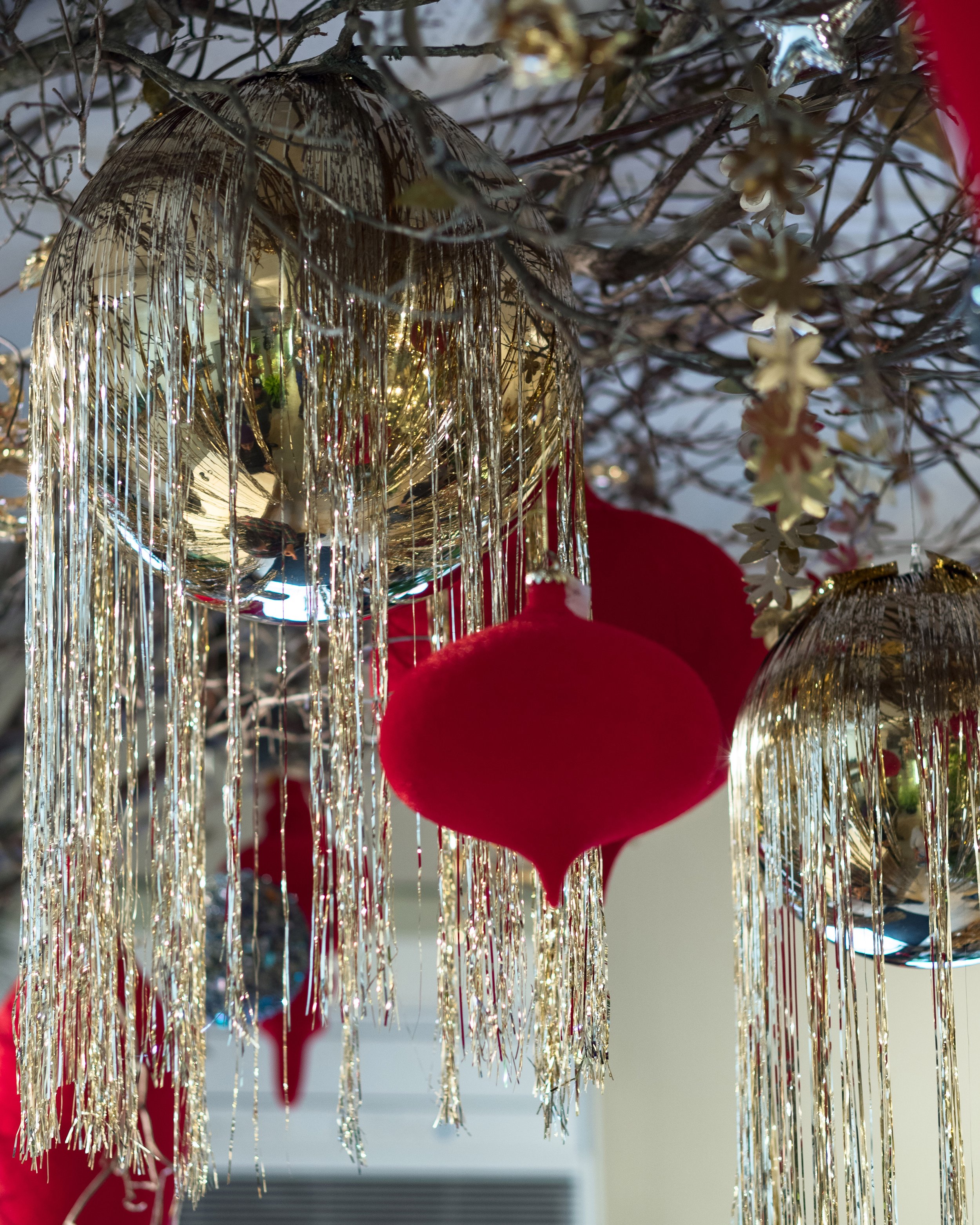 Christmas ornaments hanging from a decorated tree, featuring shiny silver globes with hanging silver tinsel and red felt ornaments in the shape of hearts.
