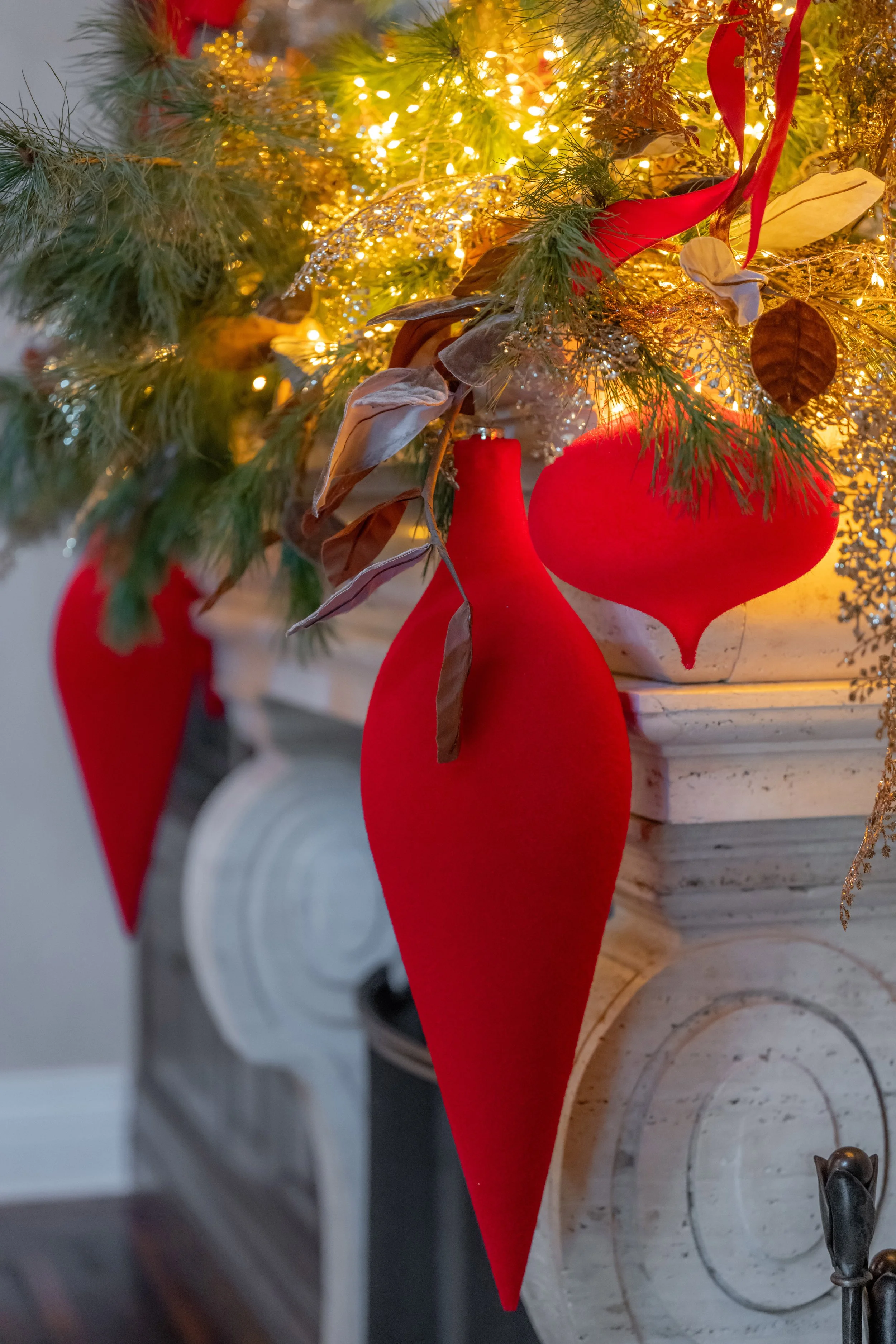 Close-up of a Christmas wreath decorated with red felt ornaments hanging from a mantle with festive string lights.