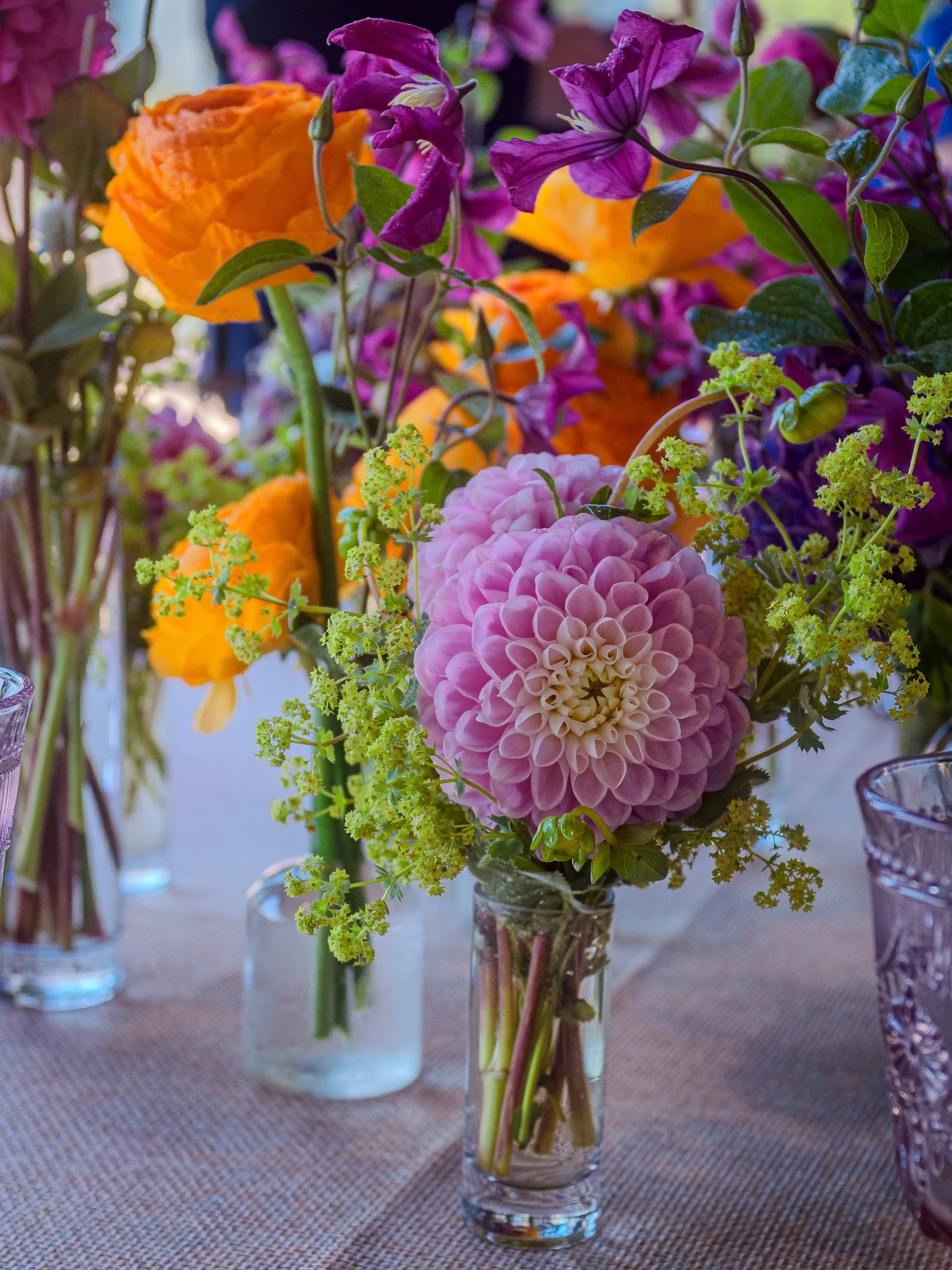 Colorful floral arrangement with pink, orange, purple, and yellow flowers in small glass vases on a table.