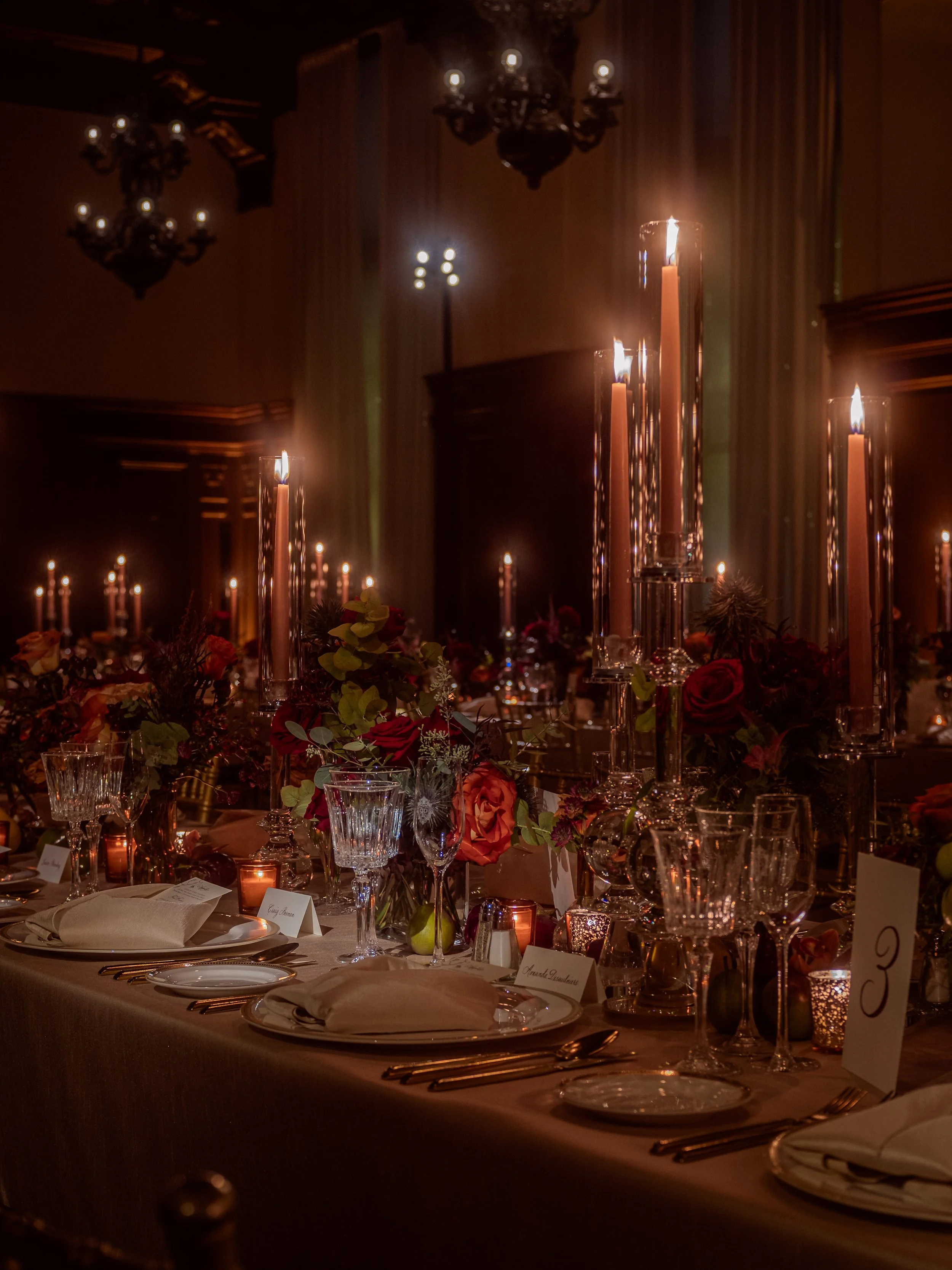 Elegant banquet table with tall candles and floral centerpieces in a dimly lit room.