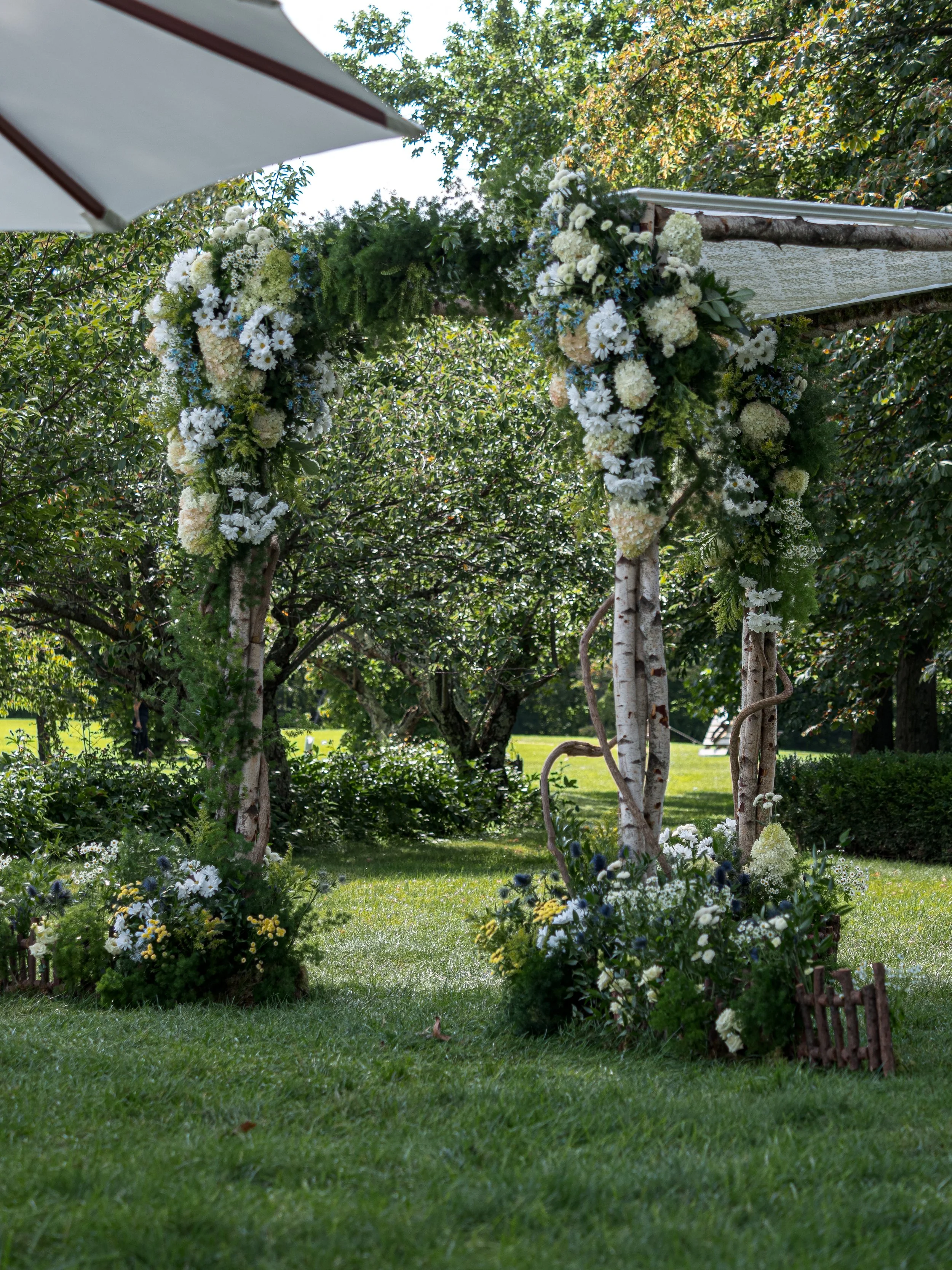 Wedding ceremony arch decorated with white flowers and greenery in an outdoor garden setting.