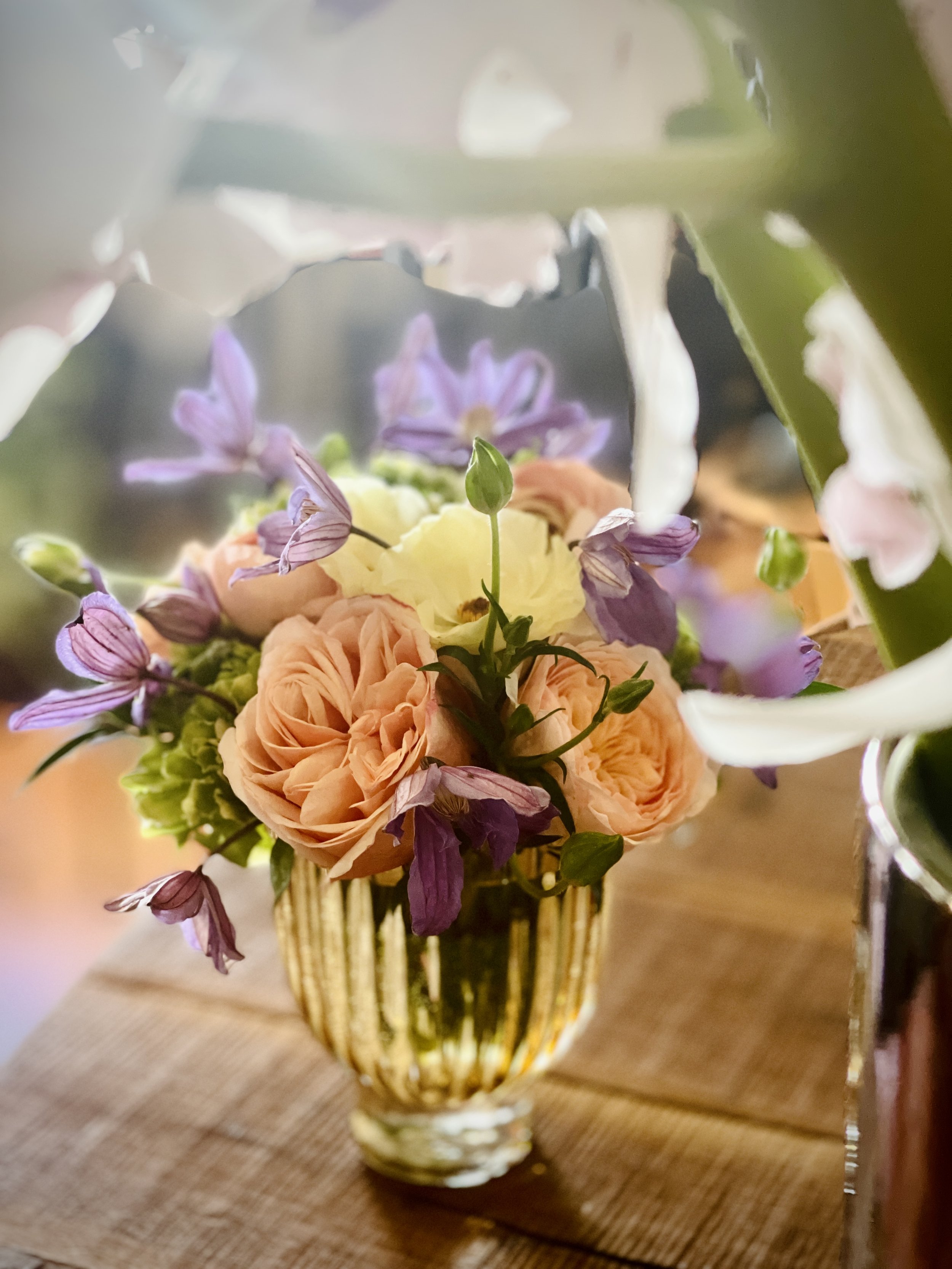 A bouquet of peach, yellow, and purple flowers in a glass vase on a wooden table.