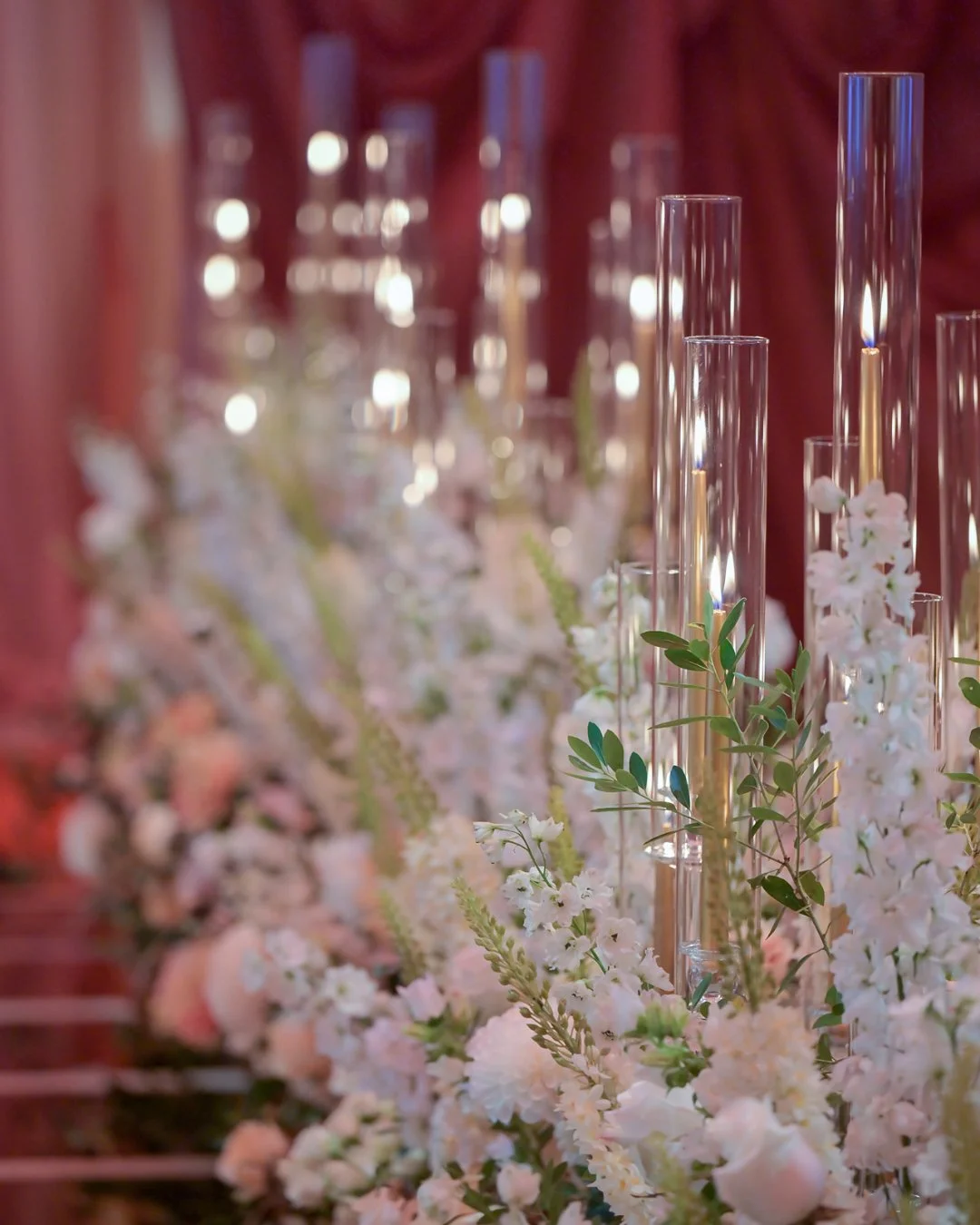 Elegant table decorated with tall glass candle holders, white flowers, and green foliage for a special event or wedding.