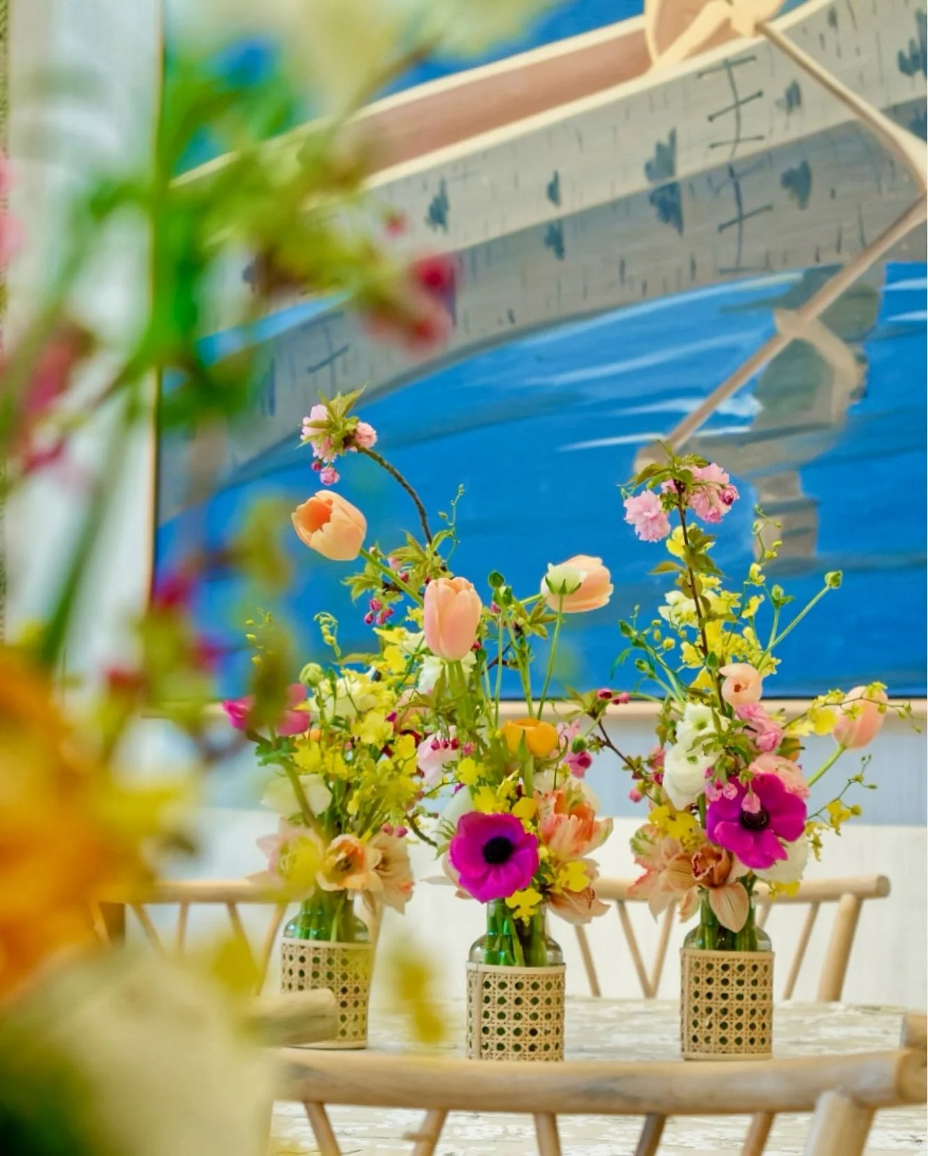 Three vases filled with colorful flowers on a table, with a large boat-themed mural in the background.