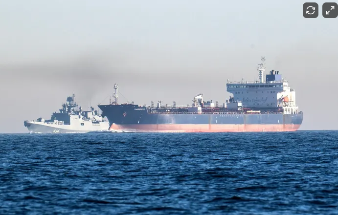 Large cargo or tanker ship sailing in open water with a smaller boat nearby.