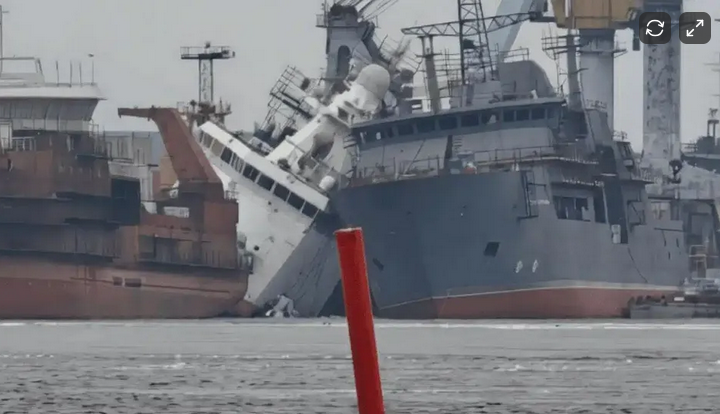 A ship is listing heavily on the water, leaning at a steep angle, with parts submerged and in immediate danger of capsizing.