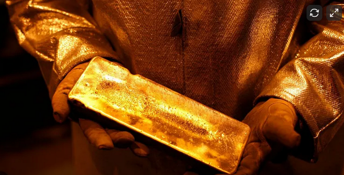 Person in a golden jacket and gloves holding a large gold brick.