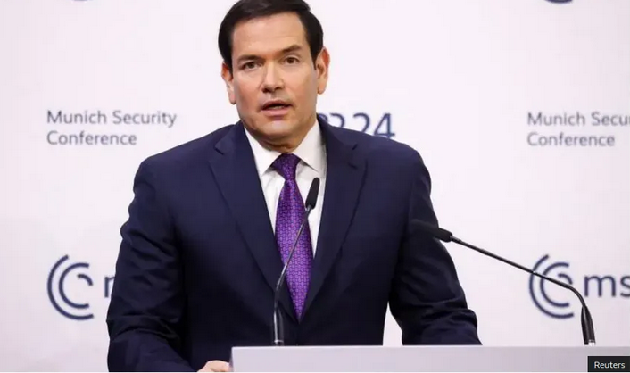 Man in a suit speaking at a podium during a conference with a backdrop that reads 'Munich Security Conference'.