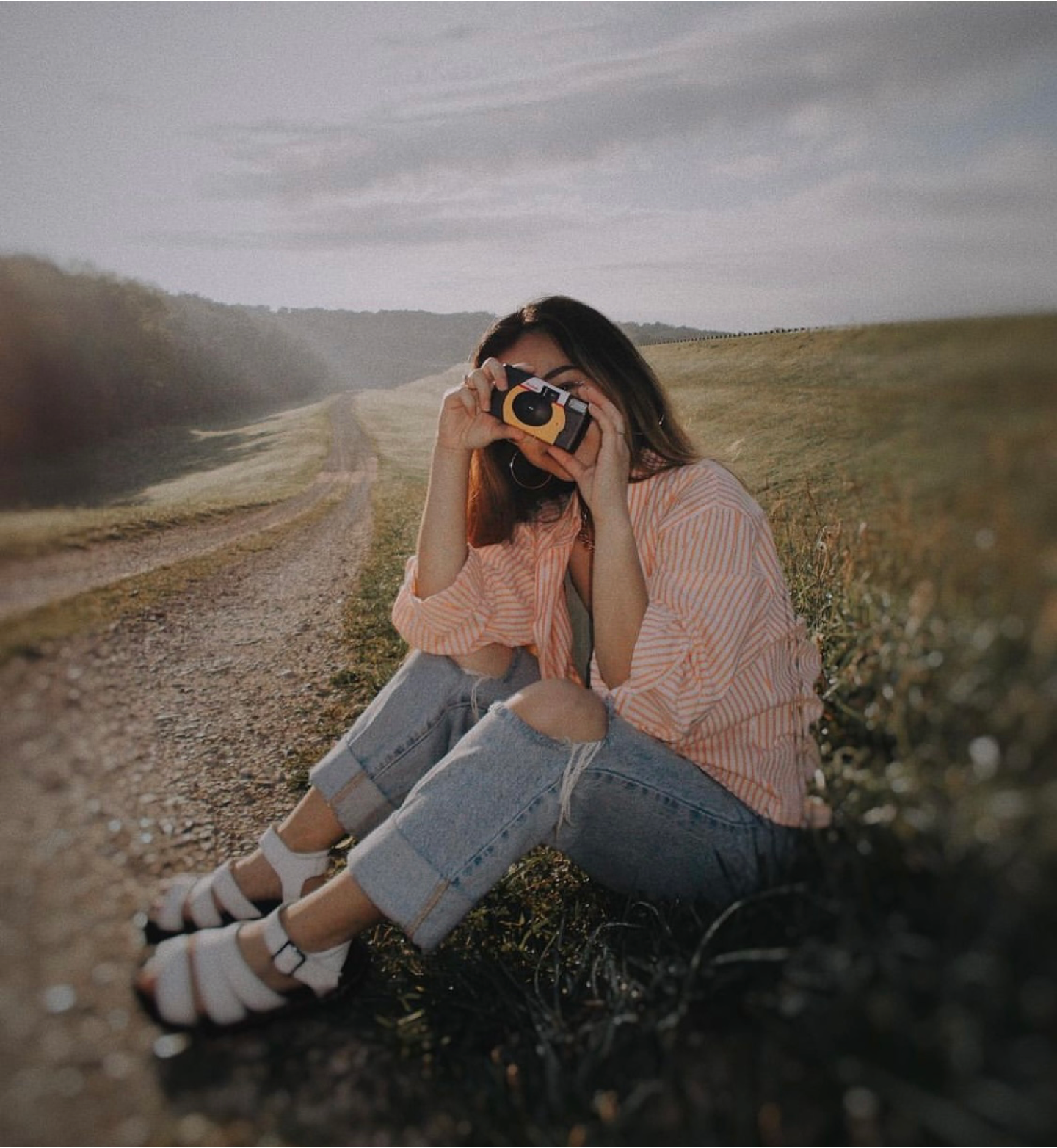 Young woman sitting on the ground, holding a disposable camera to her eye