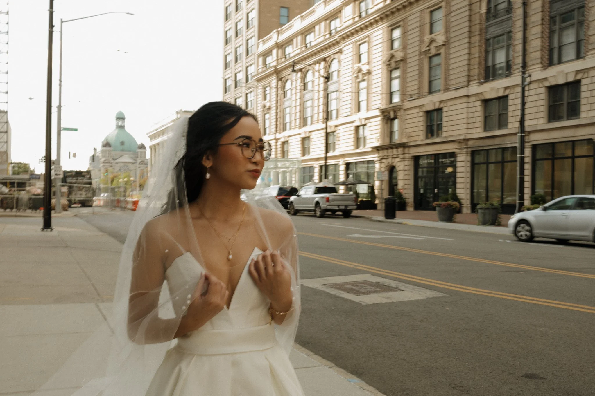 Young woman in wedding dress looking to the side of her while holder her veil on her shoulders