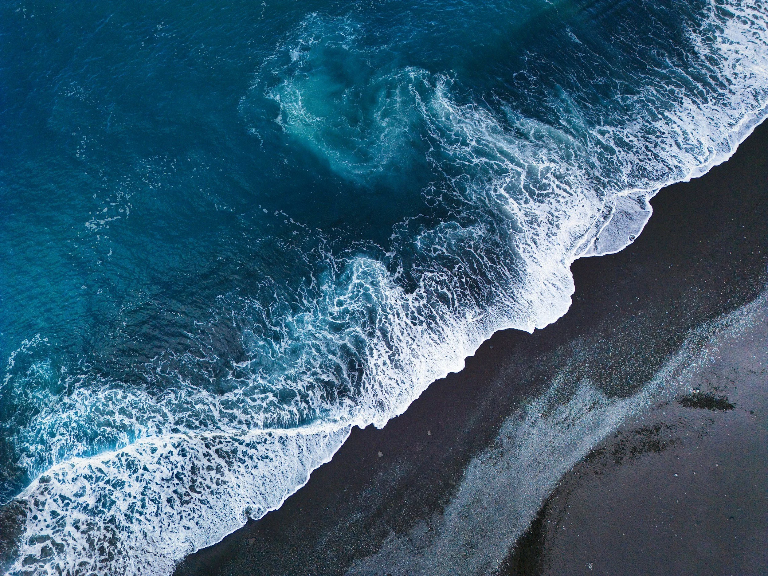 Aerial view of ocean waves crashing onto a dark sandy beach