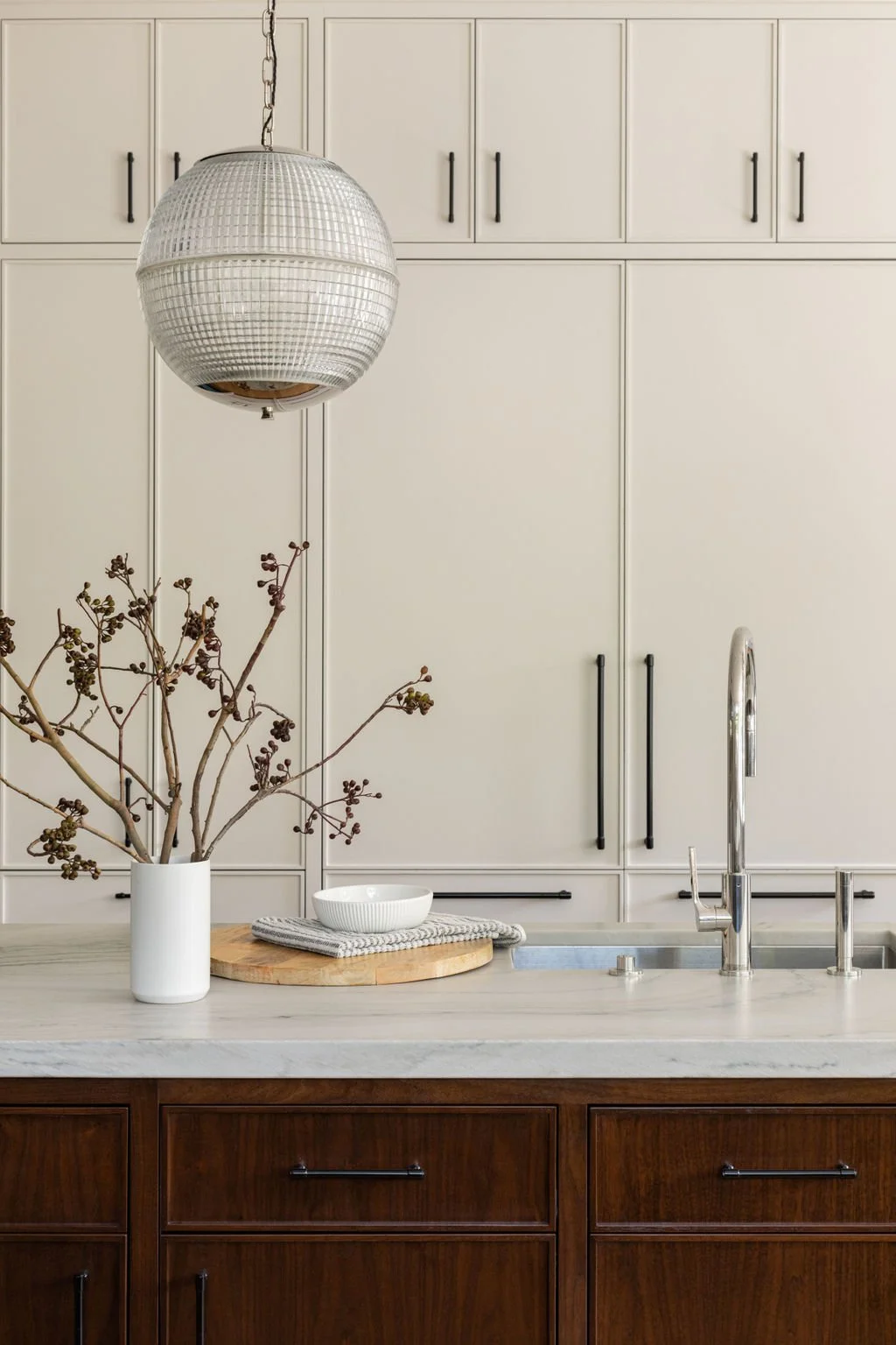 Modern kitchen with white cabinetry, a marble countertop, a hanging disco ball light, a vase with branches, a small bowl, and a sink with a chrome faucet.