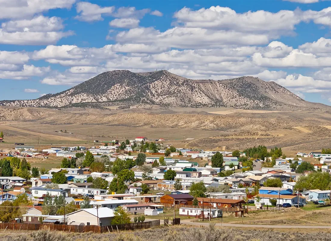 Small town beneath rugged, sparsely vegetated mountains under a partly cloudy blue sky