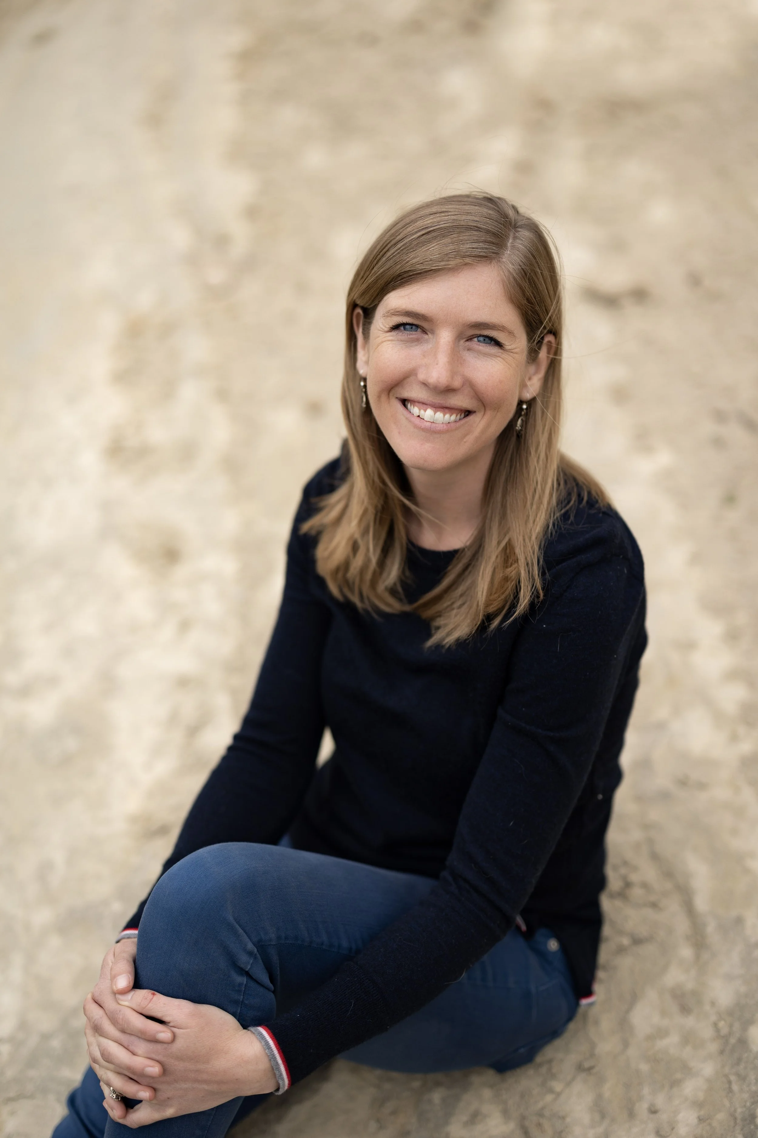 Smiling woman with long brown hair sitting against a beige stone wall