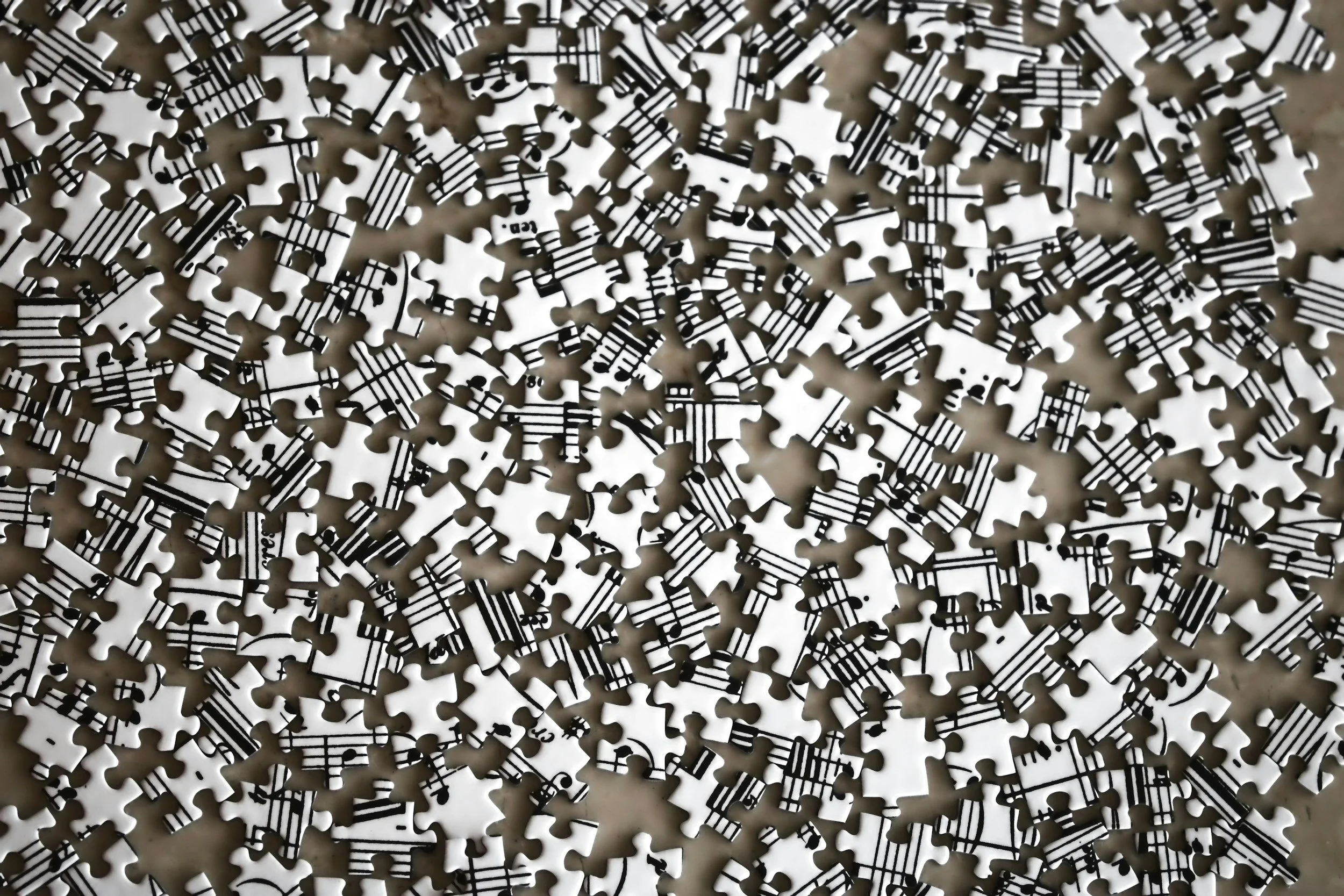 Scattered white jigsaw puzzle pieces printed with black musical notes and staff lines