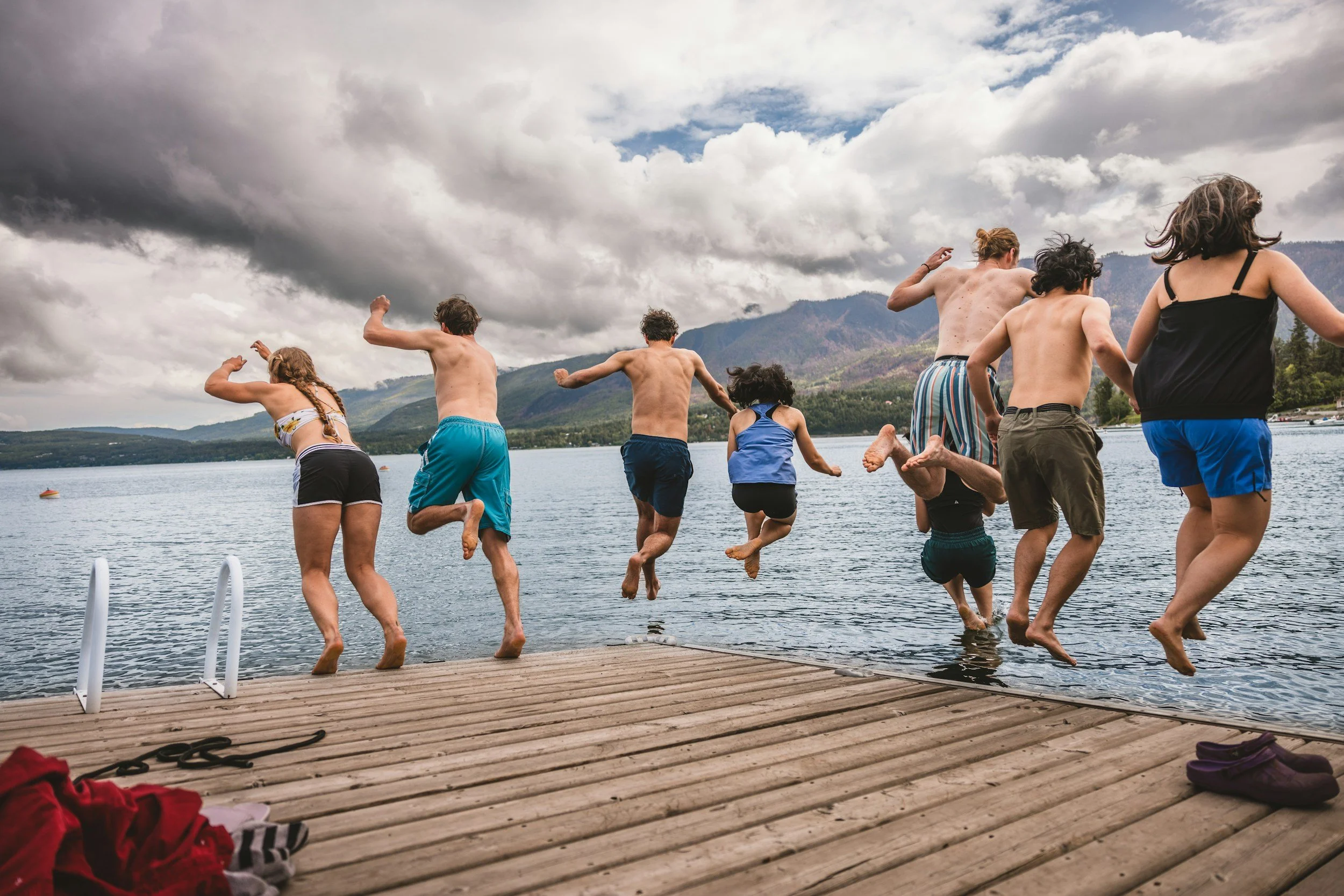 Group of friends jumping from a wooden dock into a mountain lake