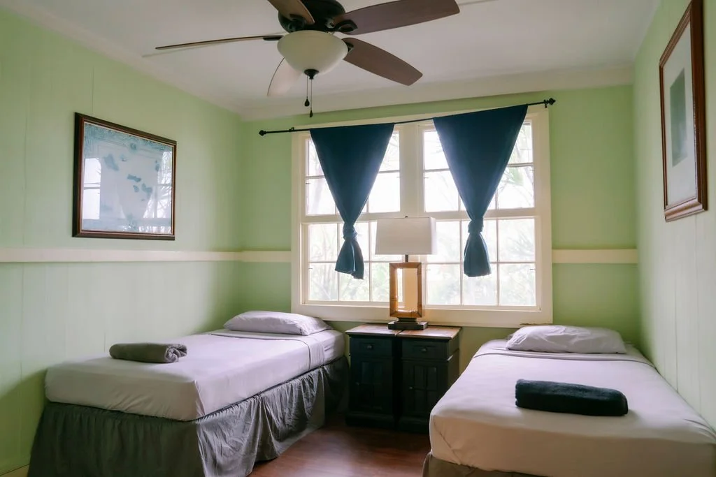 Room with two single beds, ceiling fan, and window with curtains