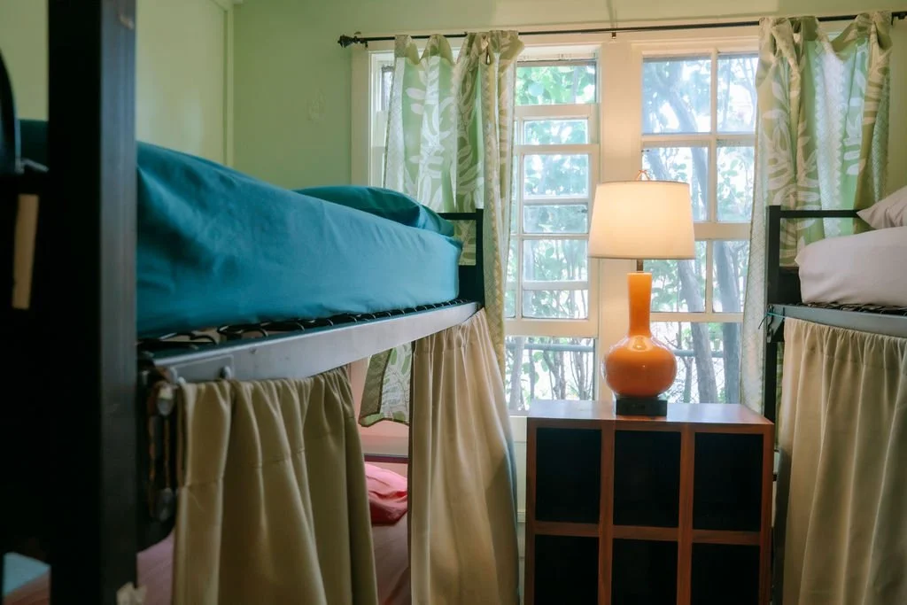 Room with two metal bunk beds, each with red bedding, tile flooring, and a window with curtains.