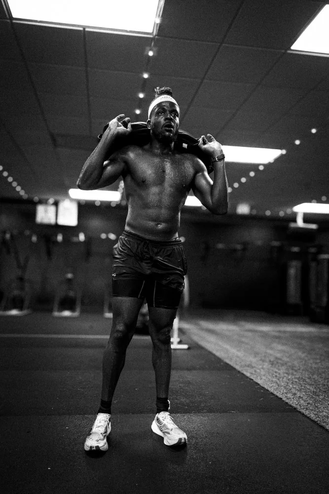 Athlete catching his breath while standing during sandbag lunges at NLXF's Hyrox Sim event, black and white photo, Des Moines