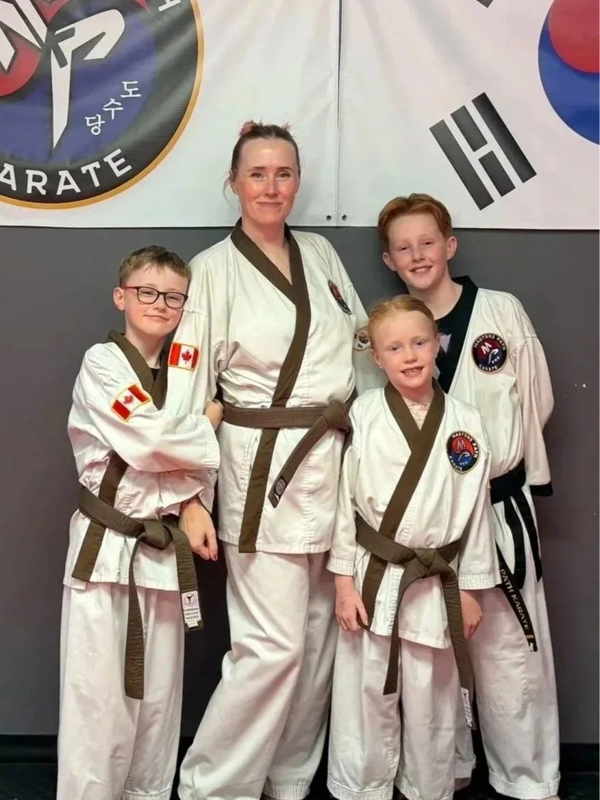 Four people in Masters Path Karate uniforms posing and smiling in front of martial arts banners.