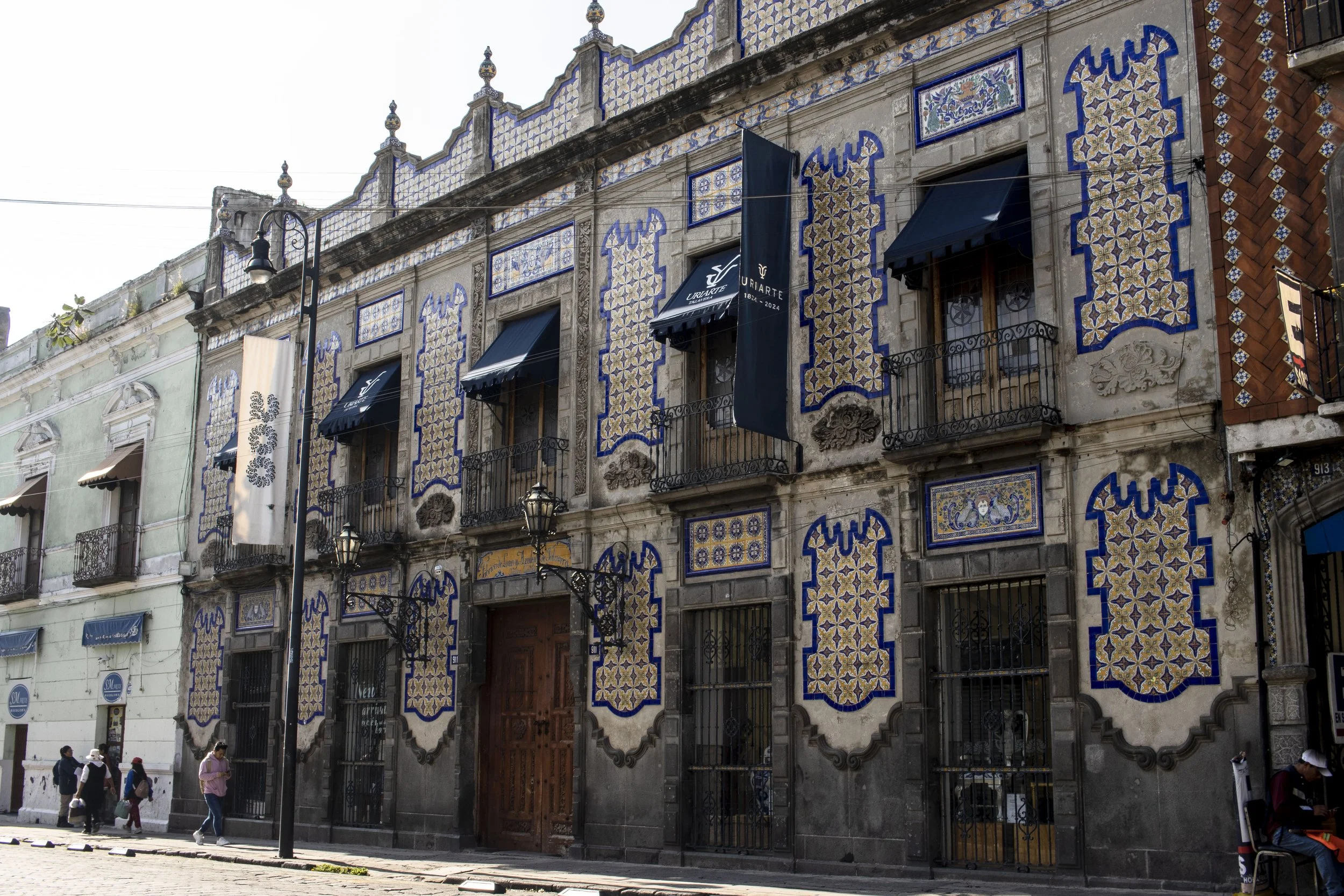 Edificio histórico con fachada decorada con azulejos de colores y balcones con rejas de hierro, en una calle de ciudad mexicana.