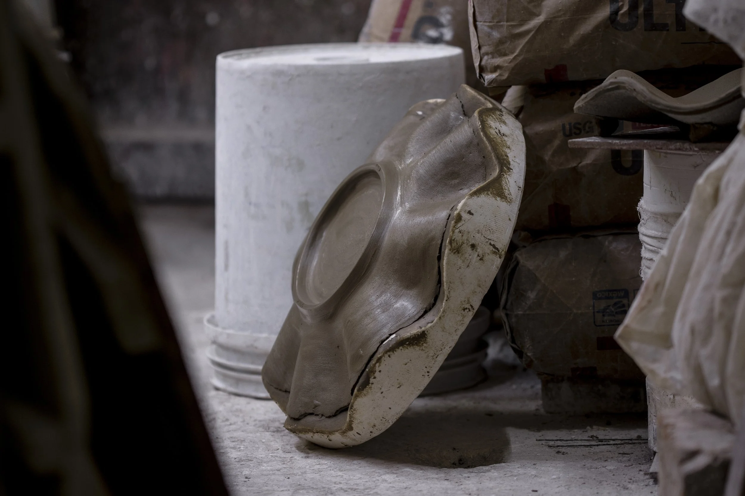 Un molde de cerámica roto con forma de boca en un taller de cerámica, rodeado de bolsas y otros materiales de cerámica.