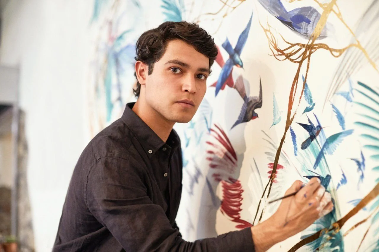 Joven hombre pintando un mural de aves en la pared.