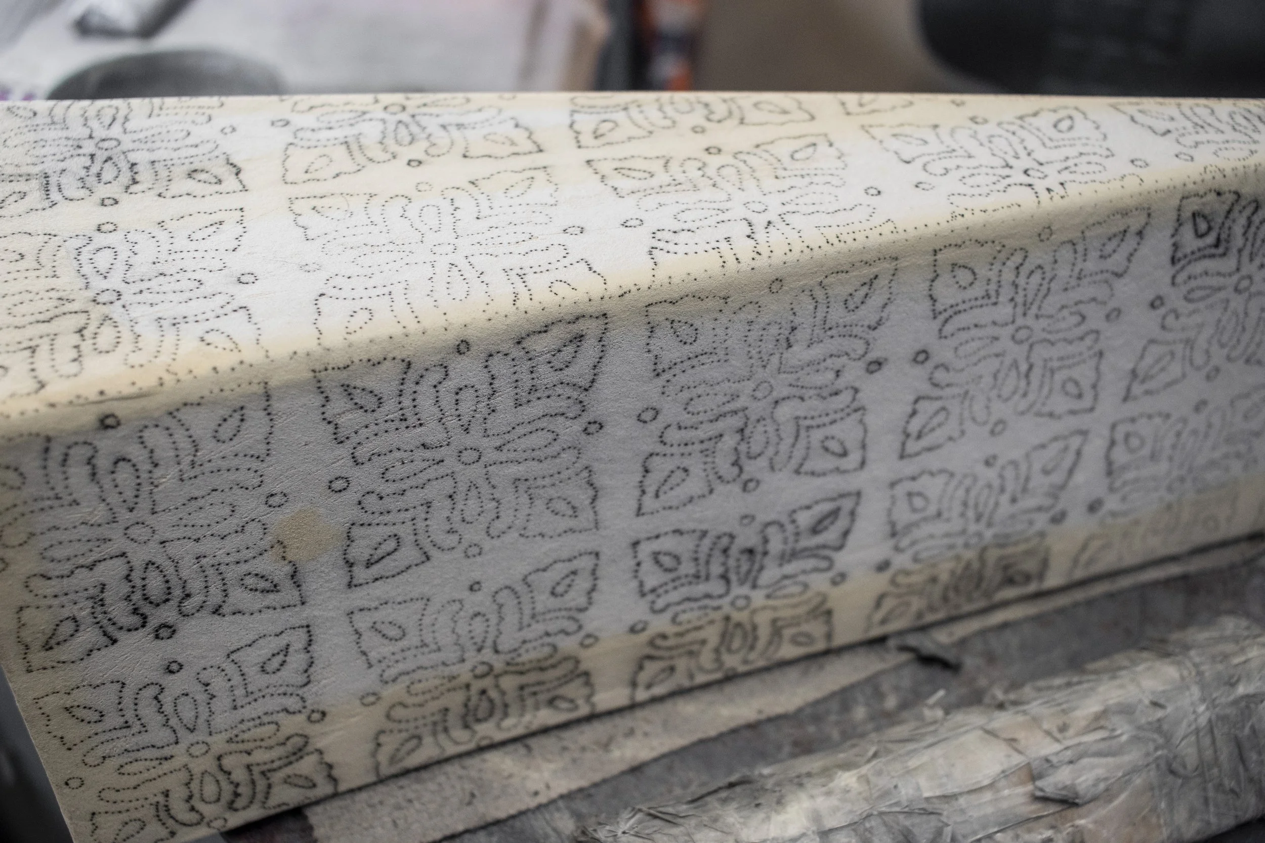 Tela con patrón de diseño en bordado en puntos en color negro sobre fondo claro, parece estar en una máquina de coser o proceso de bordado.