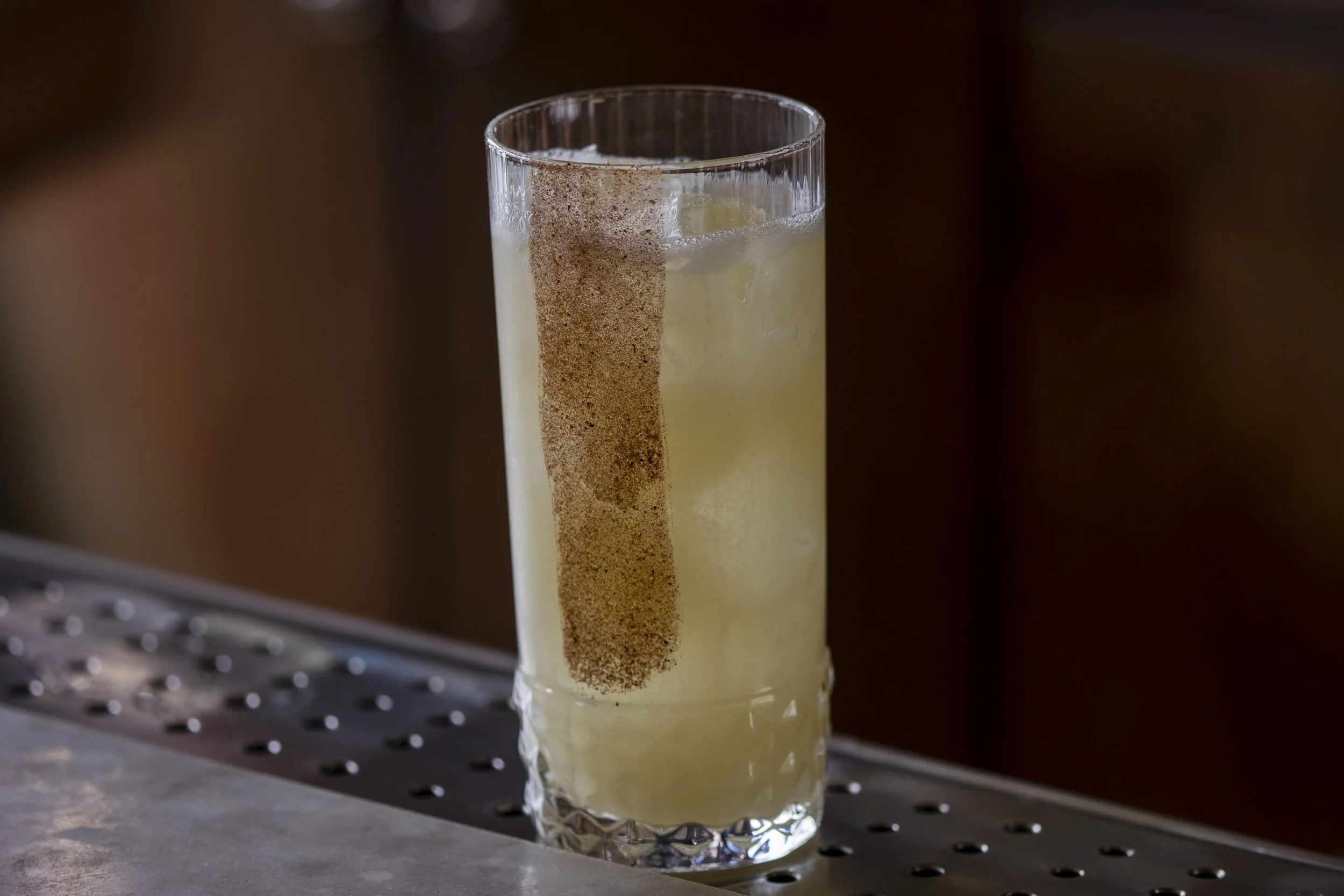 Copa de vidrio alta con bebida clara y hielo, con polvo de canela en el borde