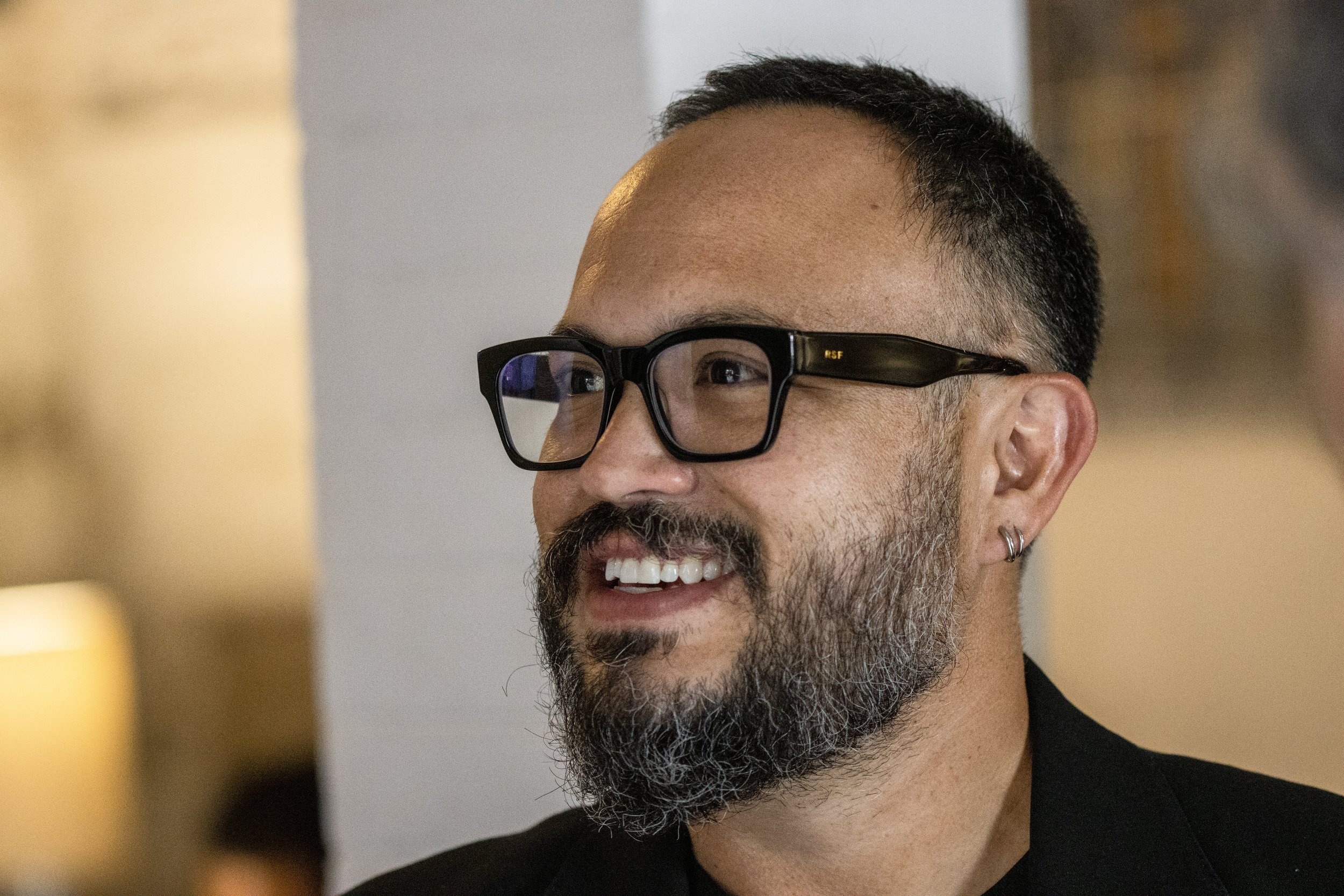 Hombre con gafas de montura negra y barba, sonriendo.