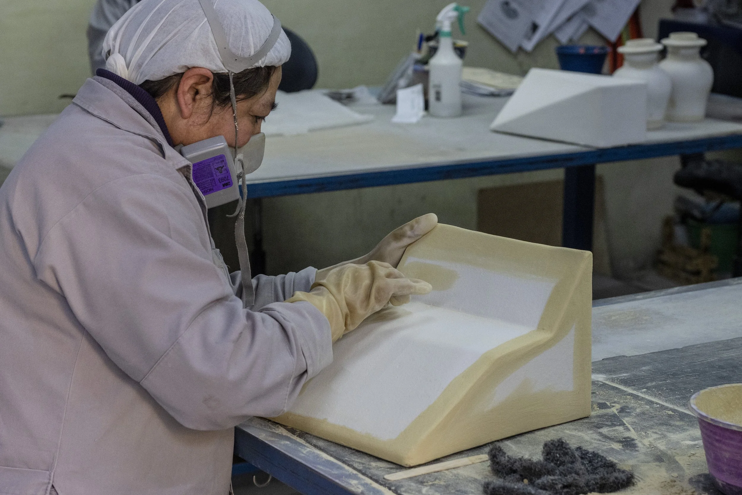 Una persona trabajando en la elaboración de un molde con silicona en un taller, usando guantes y protección respiratoria.