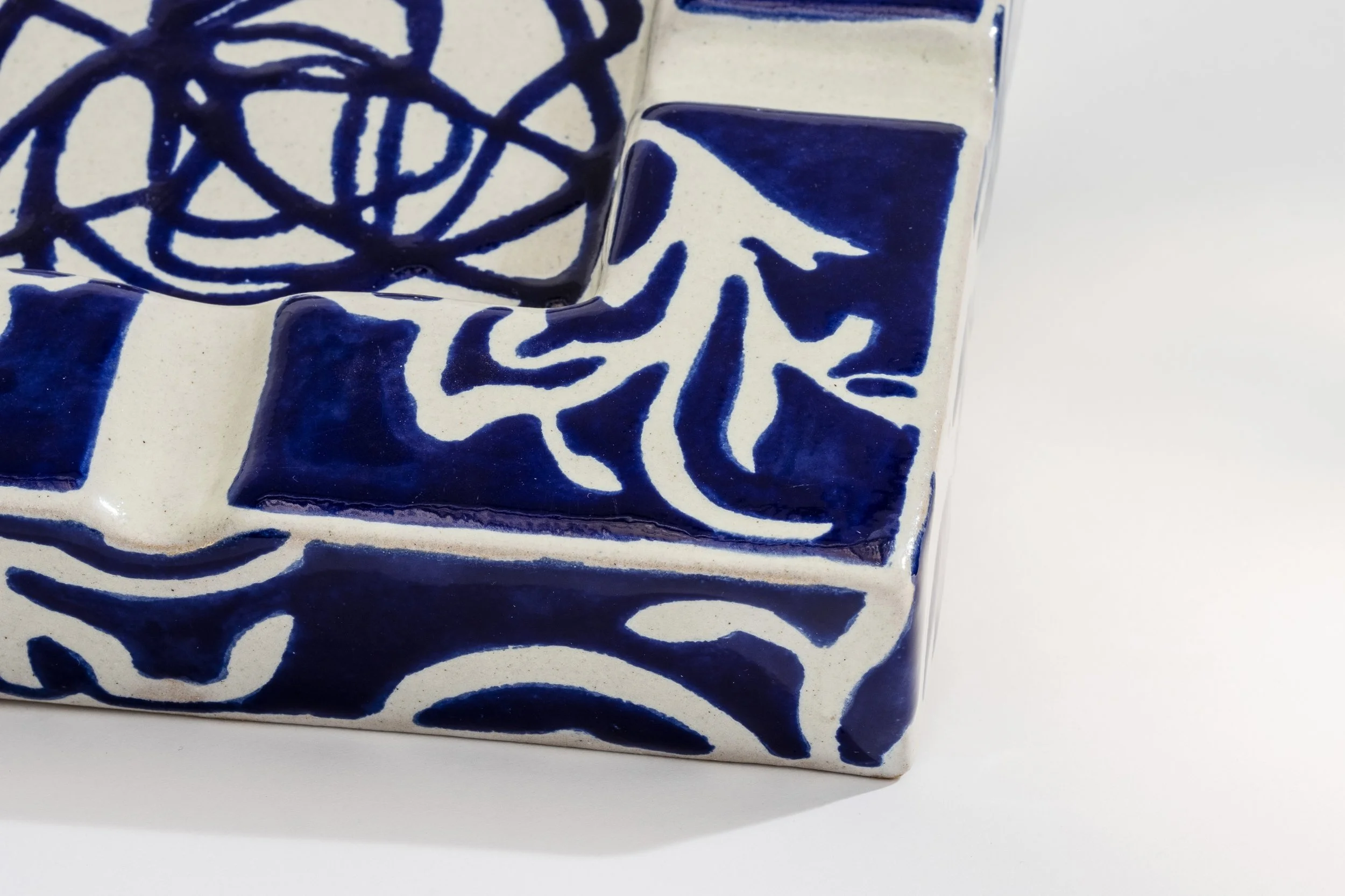 Reja de cerámica blanca con decoraciones en azul, incluyendo un diseño floral y patrones geométricos.