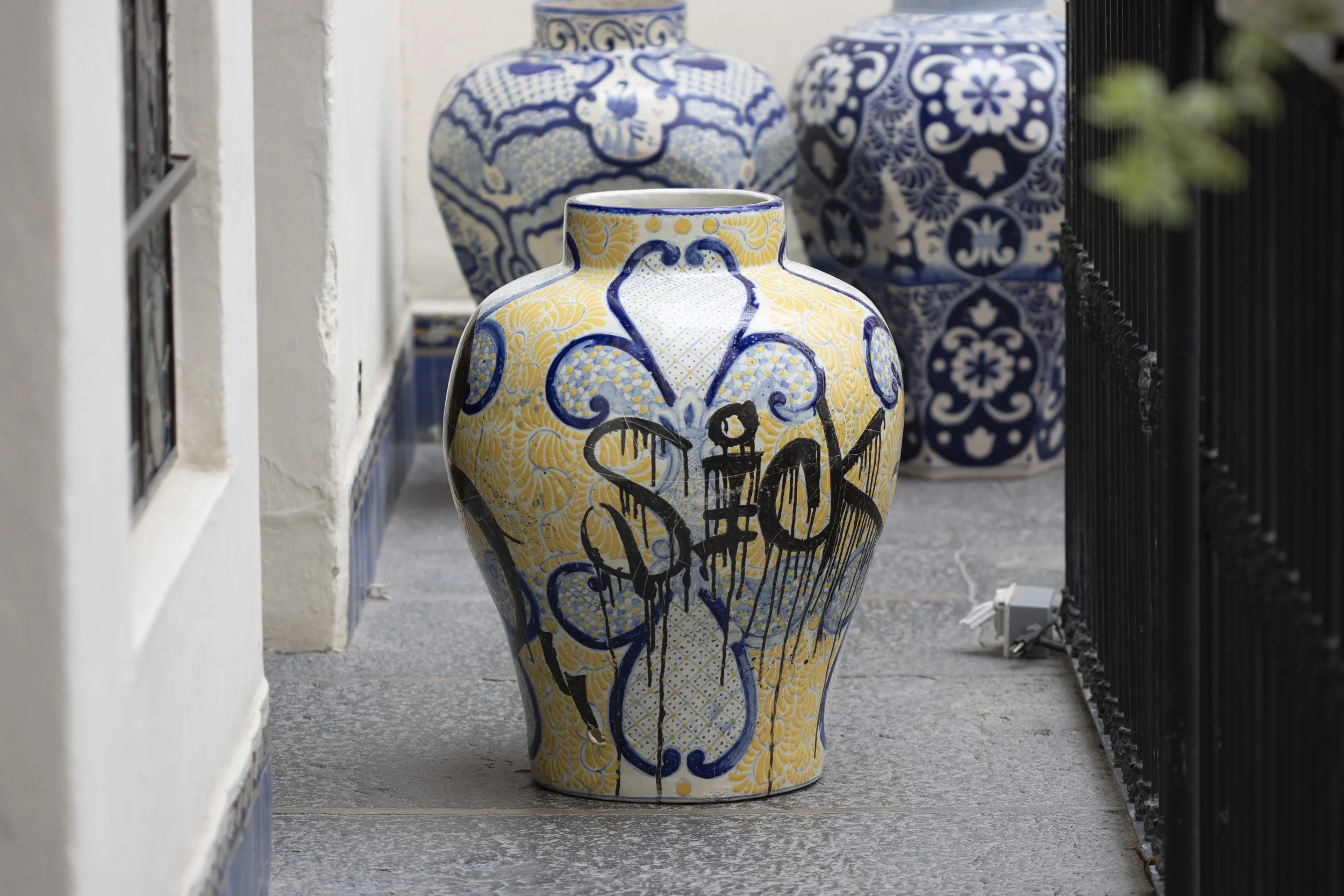 Plato decorativo con diseños abstractos y ojos en triángulos. Incluye líneas negras verticales y patrones en azul y amarillo sobre fondo blanco.