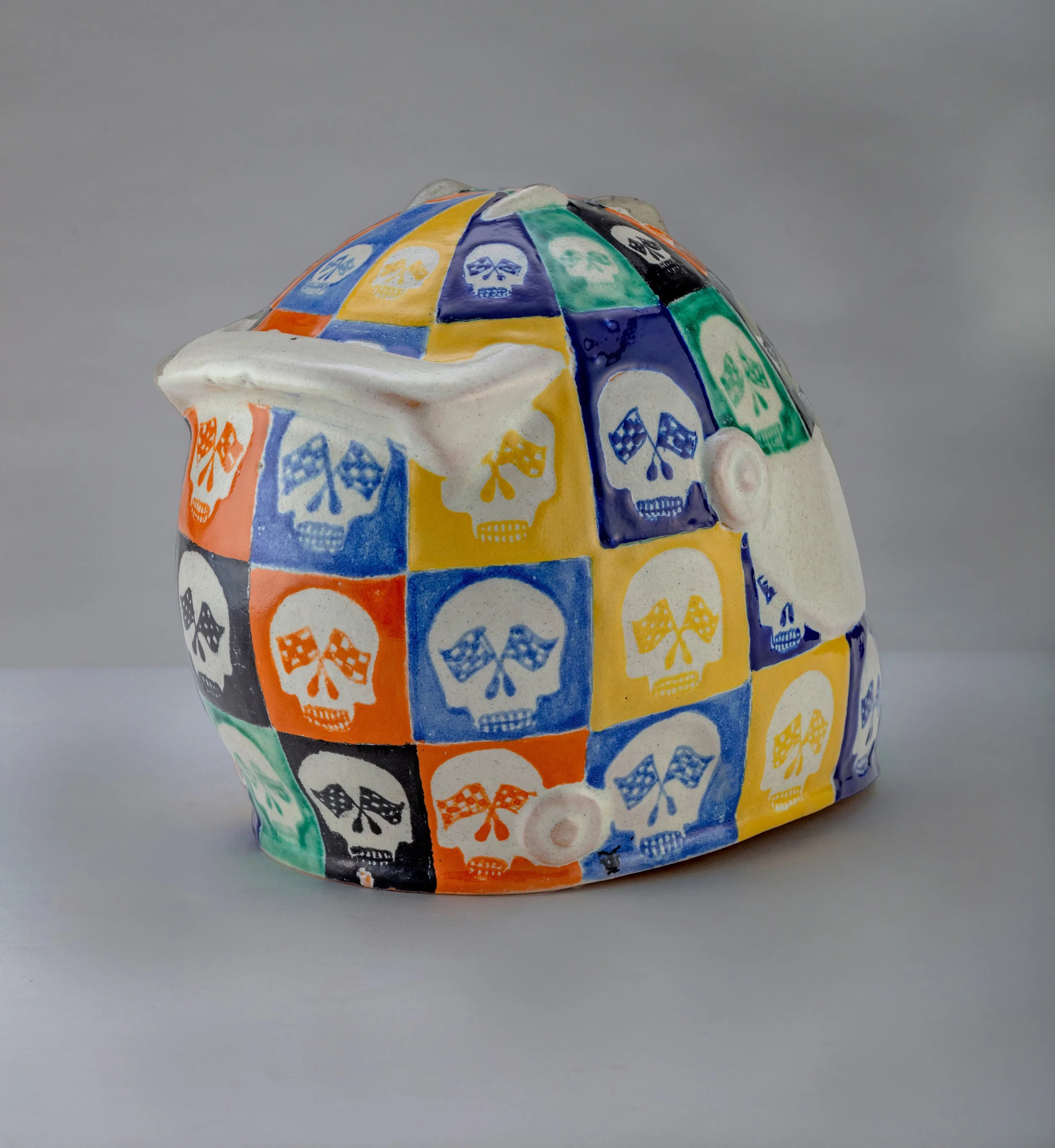 Escultura de cerámica con patrón de calaveras y banderas en colores amarillos, azules, verdes, naranjas, y negros.