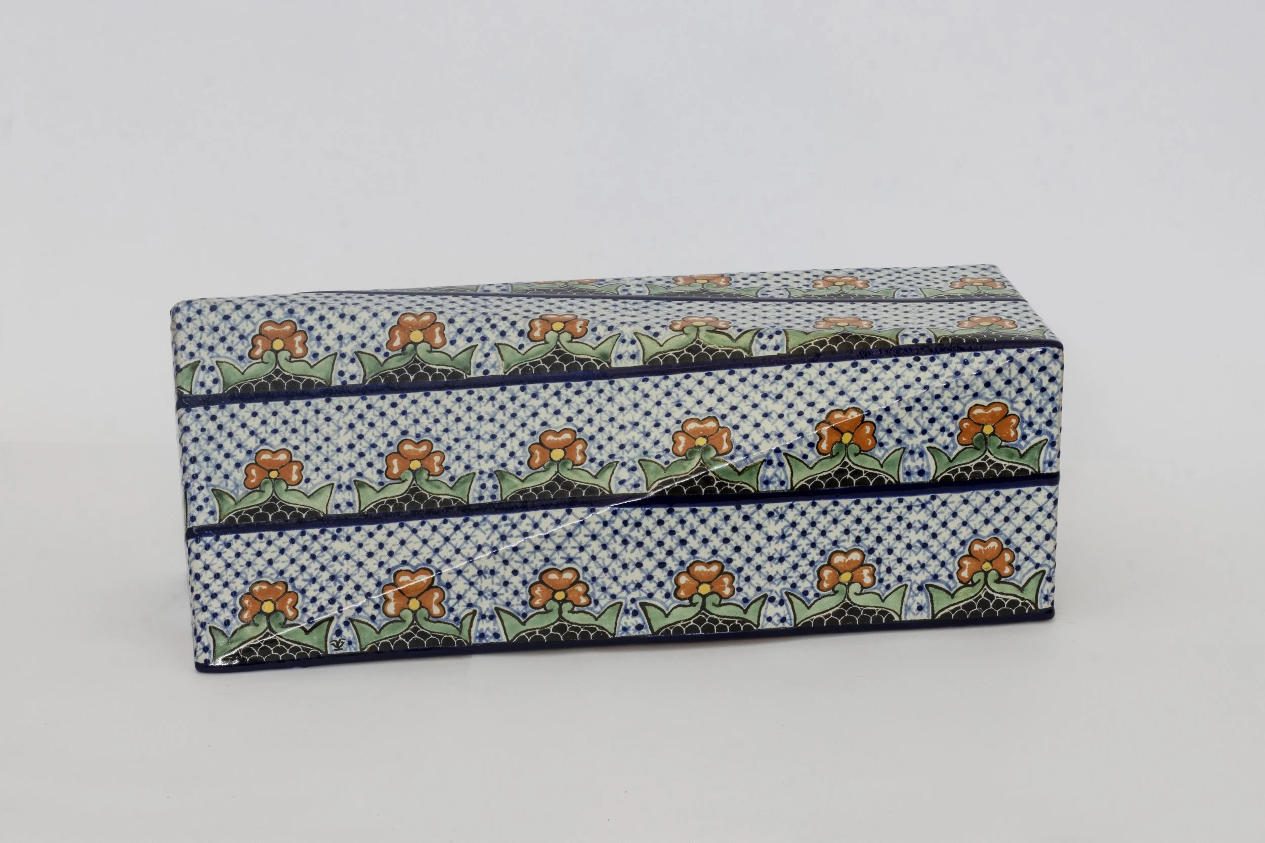 Cajita decorativa con diseño floral en tonos verdes, naranjas y negros sobre fondo azul con puntos blancos