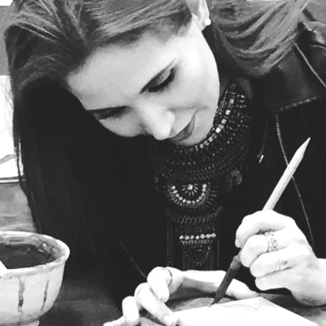 Mujer escribiendo con un pincel en una mesa, en un ambiente artístico, en blanco y negro.