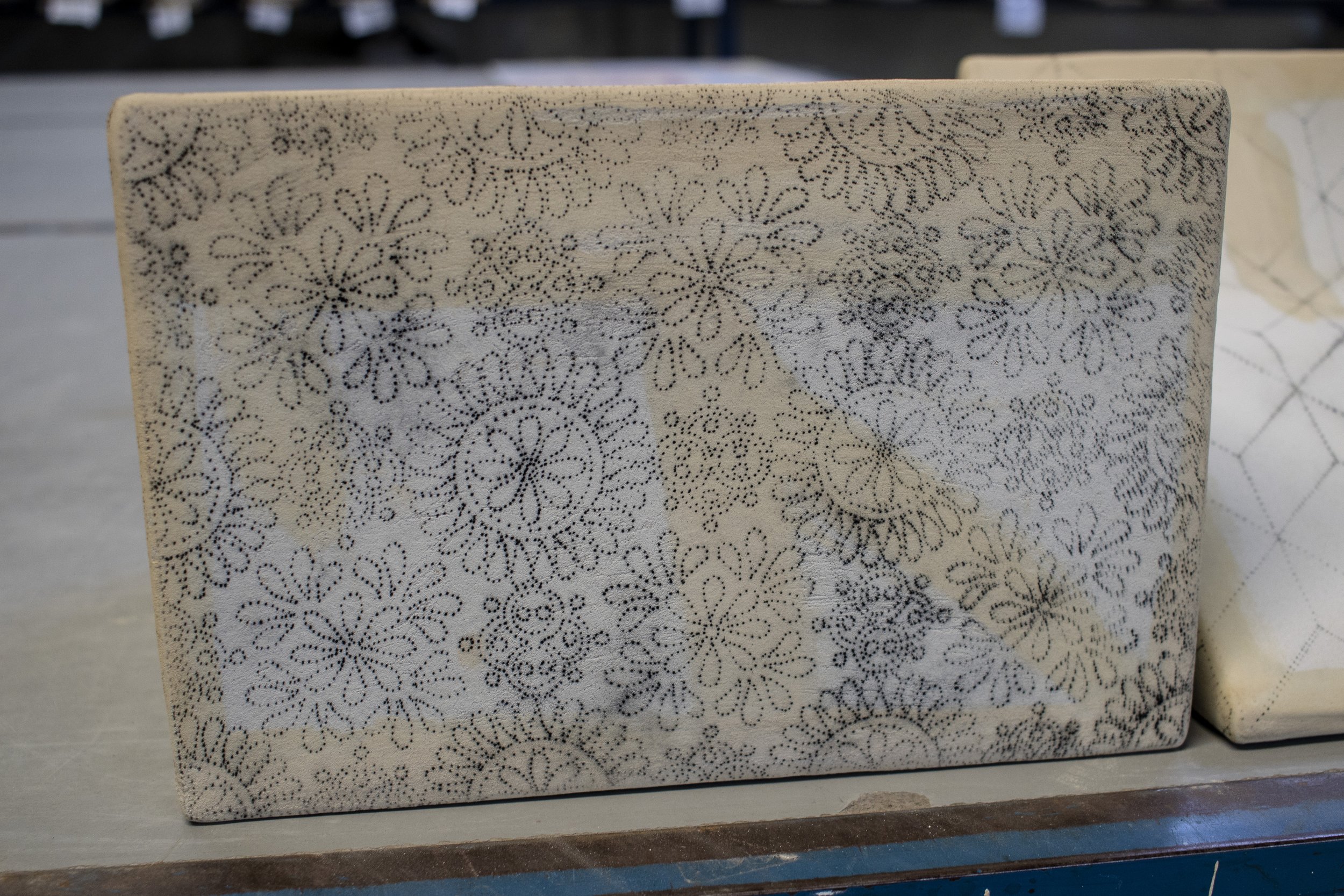 Pieza decorativa rectangular con patrón de círculos y formas florales en tonos negro y beige.