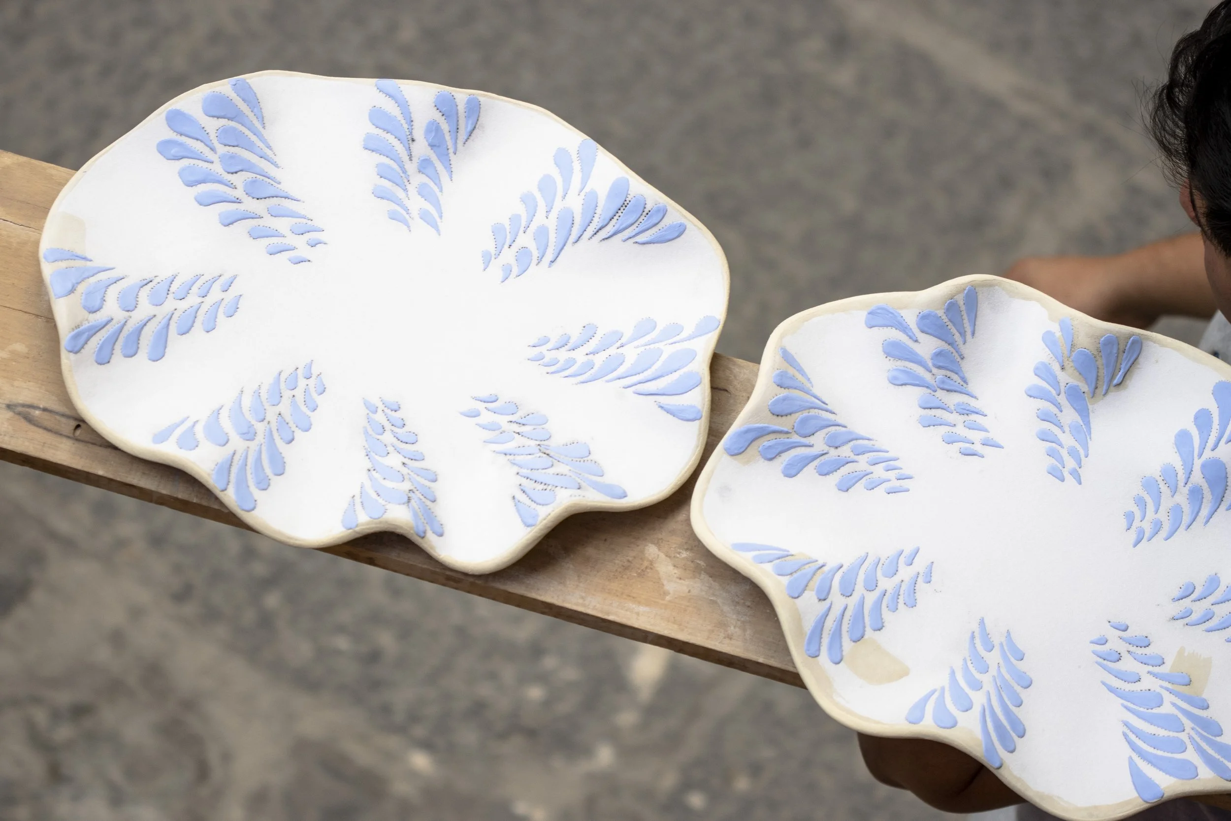 Platos de cerámica con diseño de hojas azules sobre fondo blanco, colocados sobre una mesa de madera.