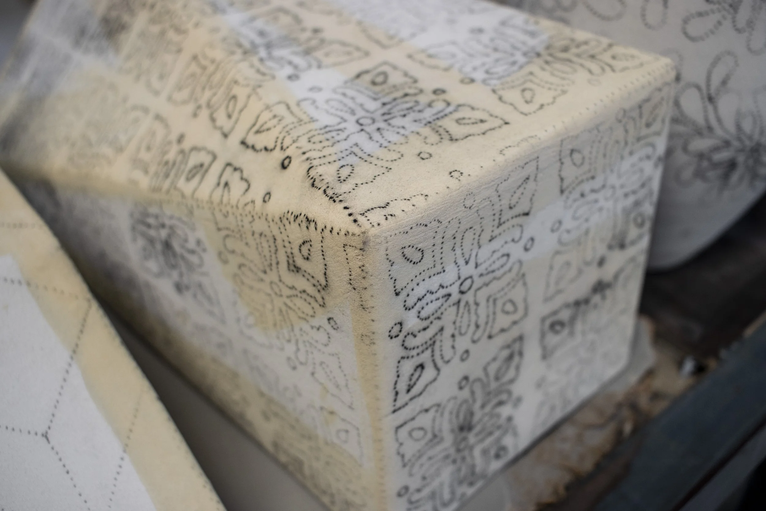 Madera pintada con patrón decorativo en colores claros y detalles en negro.