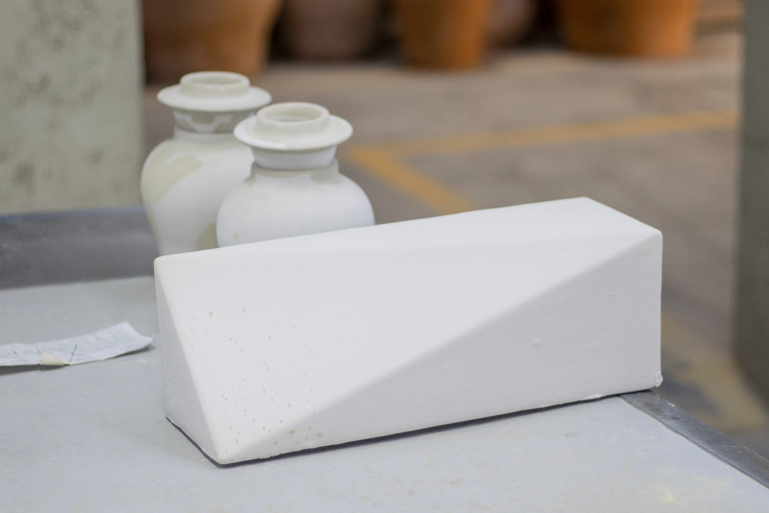 Cuña de esponja y frascos blancos sobre una mesa en un entorno industrial o de almacenamiento.