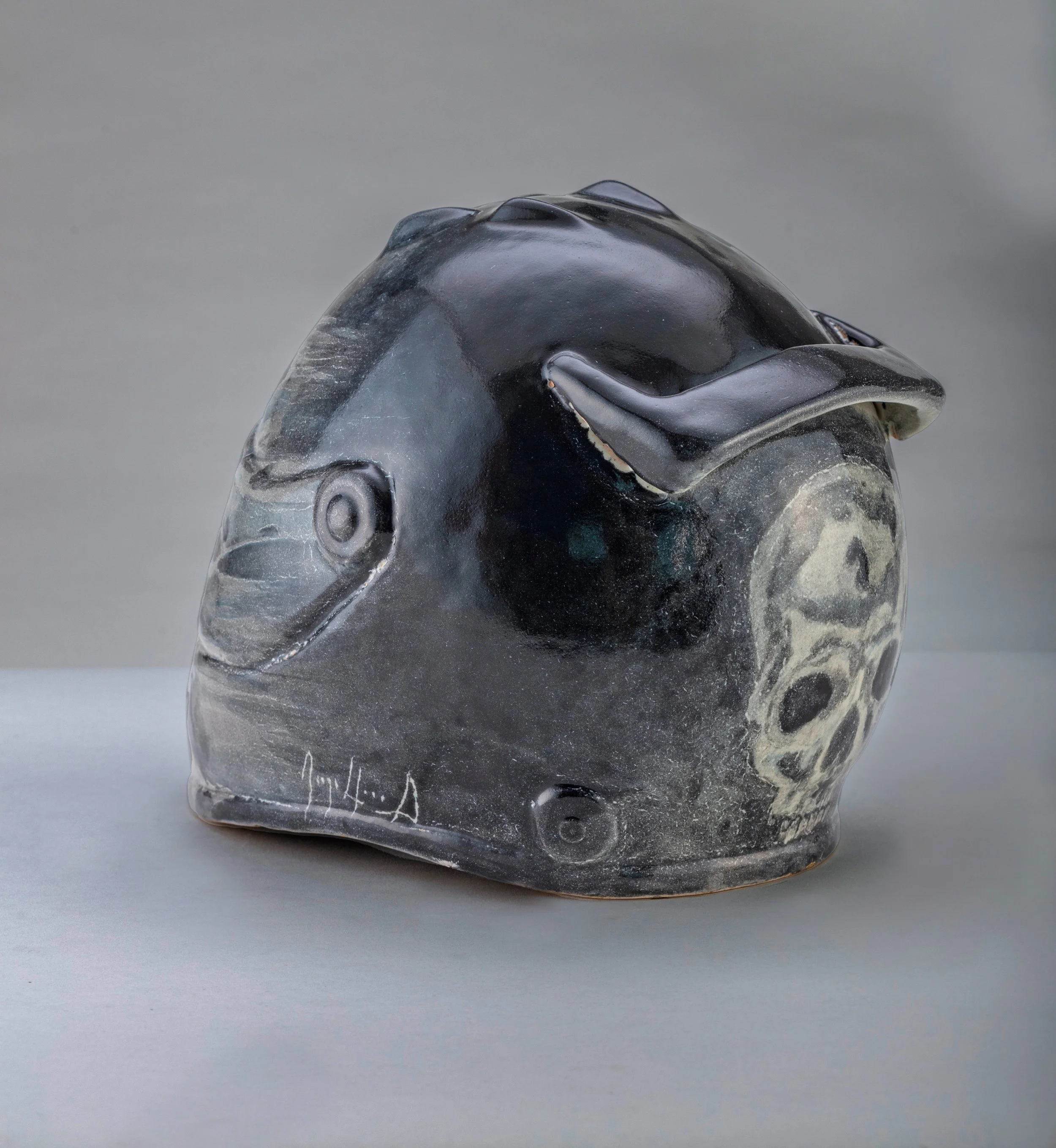 Escultura de cerámica en forma de calavera con diseño de pez en tonos oscuros y superficie brillante.