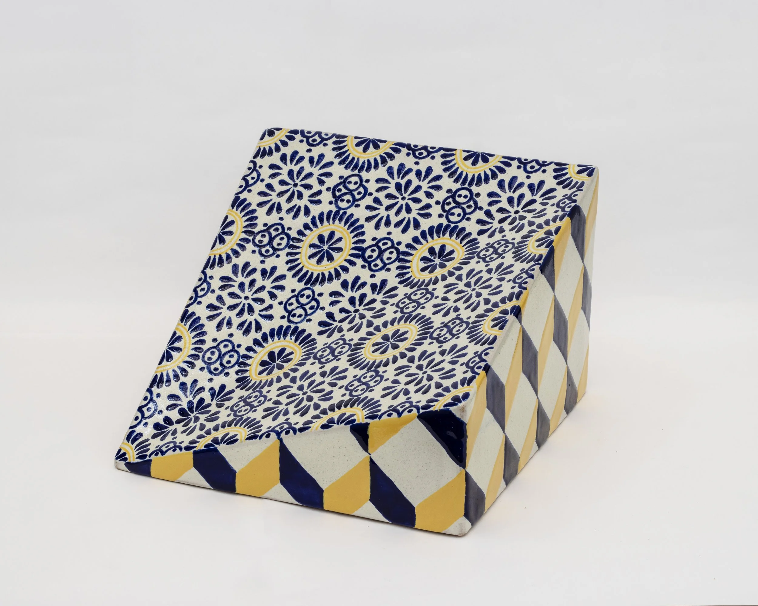 Bandeja decorativa de cerámica con patrones azules, blancos y amarillos, con un diseño en forma de prisma rectangular.