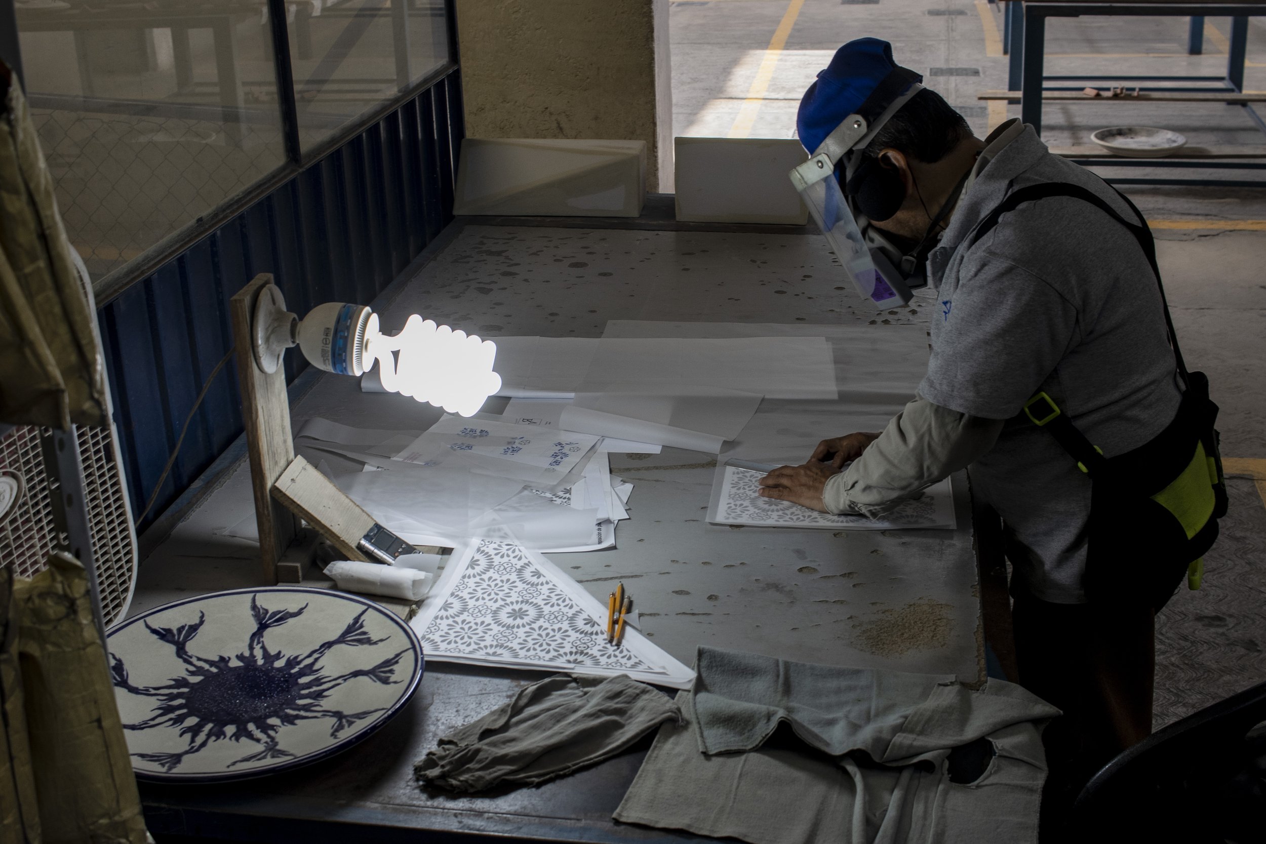 Artesano trabaja en su taller, pintando y decorando cerámica. Hay varias piezas de cerámica y herramientas en la mesa.