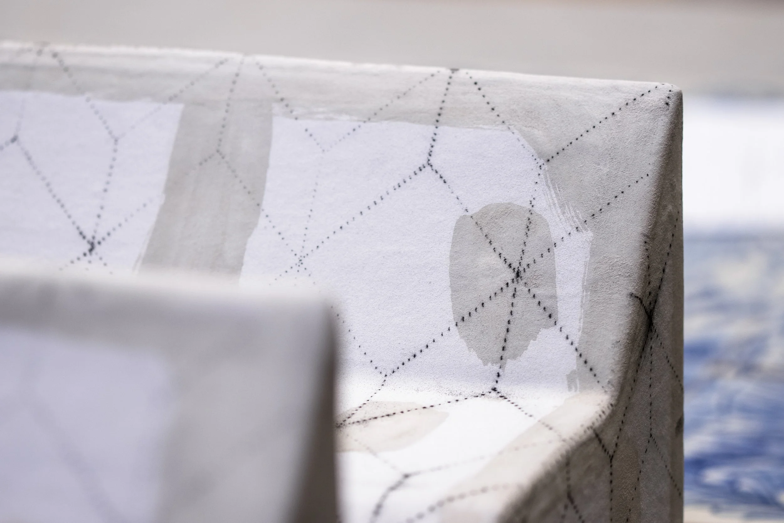 Una silla con tapizado blanco que tiene un patrón de cuadros con puntos y líneas, ubicada cerca de una piscina o cuerpo de agua.