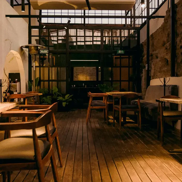 Interior de un restaurante con muebles de madera, paredes de piedra y estructura de metal, iluminado cálidamente.