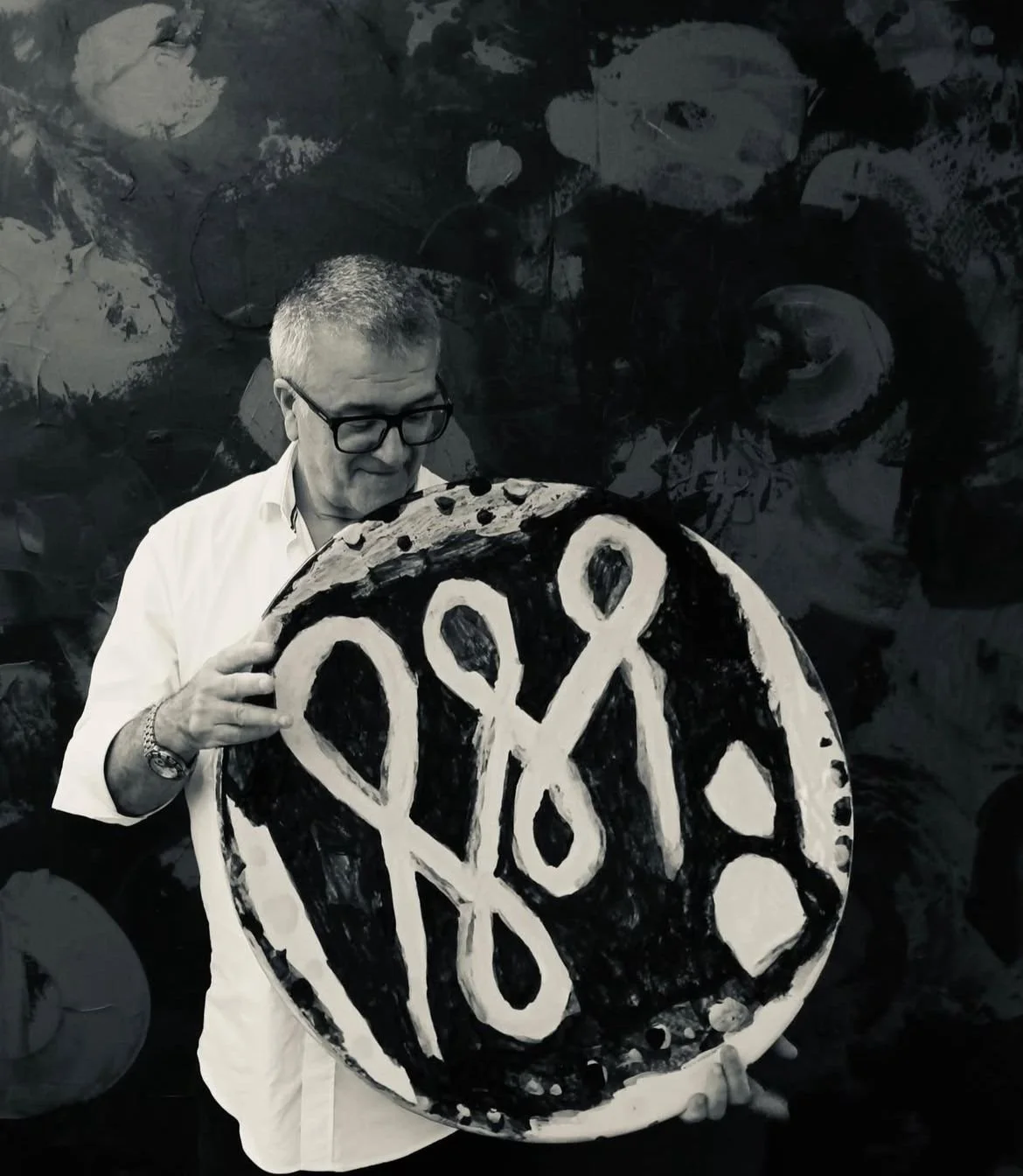 Hombre con gafas sostiene una obra de arte circular con formas abstractas en blanco y negro.