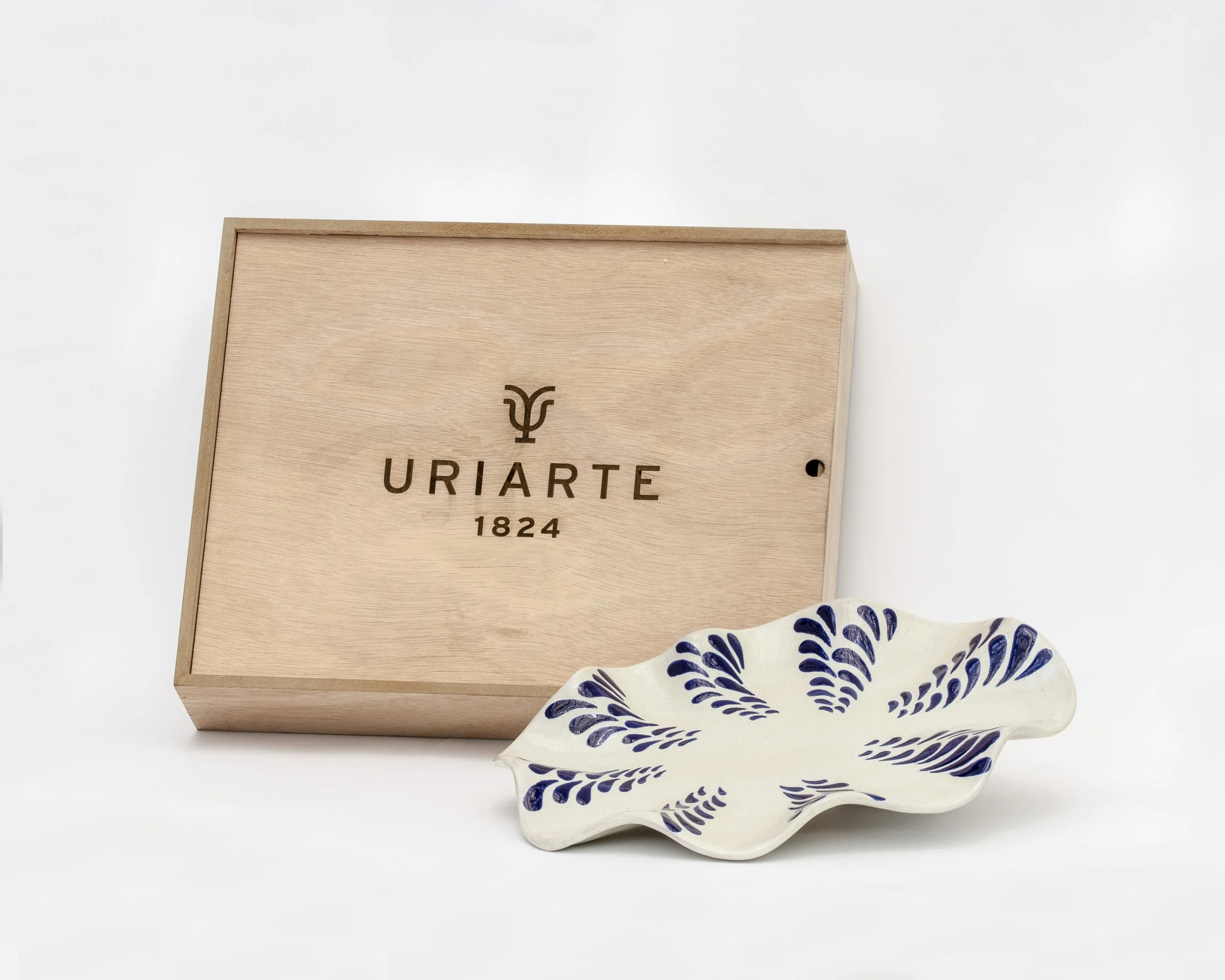 Un plato decorativo de cerámica con diseños en azul y una caja de madera con marca 'URIARTE 1824'